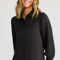 Woman wearing a black shirt and beige pants against a white background