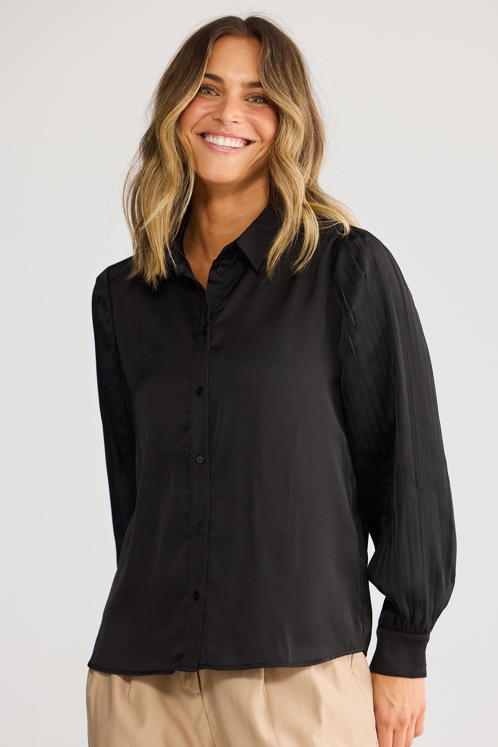 Woman wearing a black shirt and beige pants against a white background