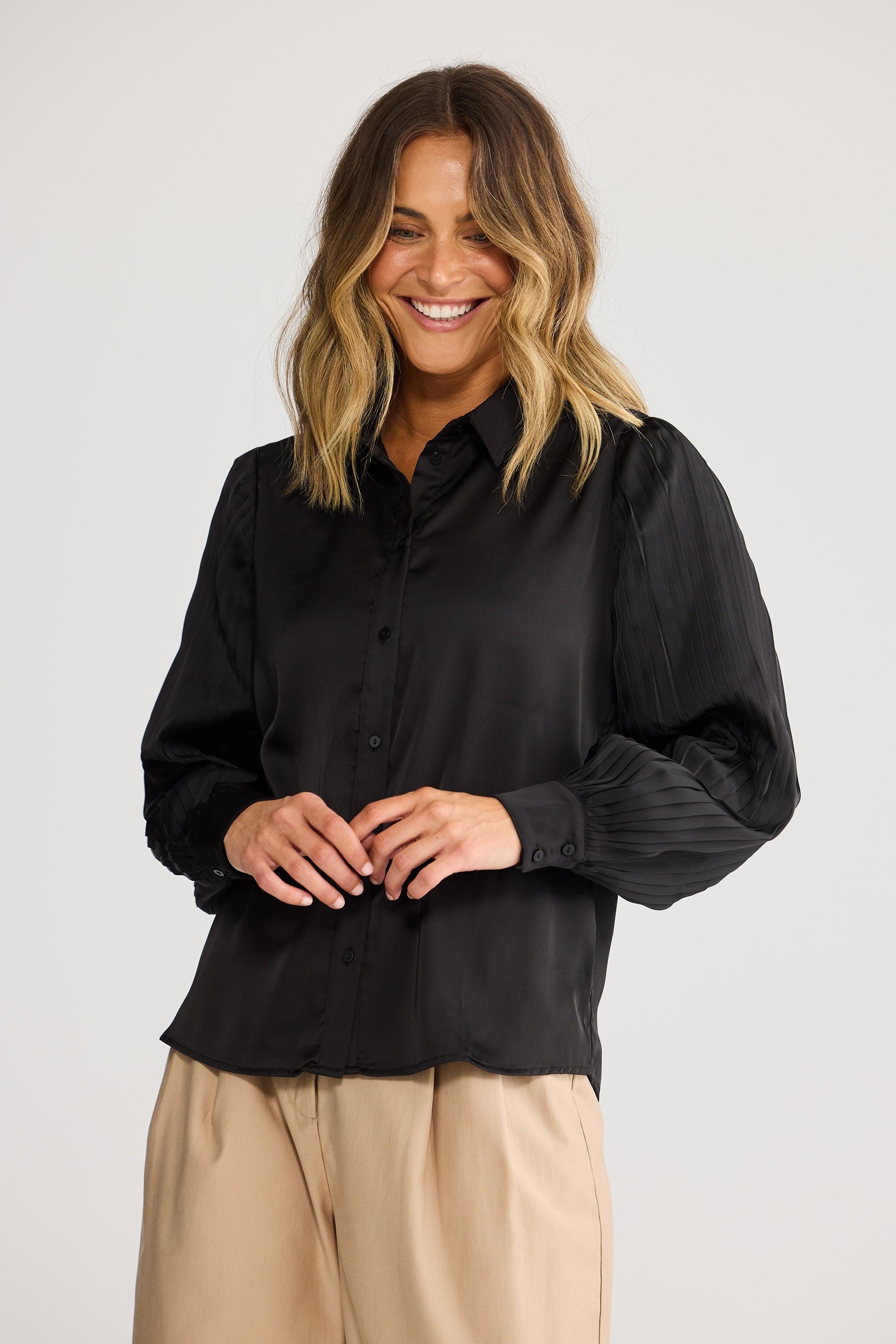 Woman wearing a black shirt and beige pants against a white background