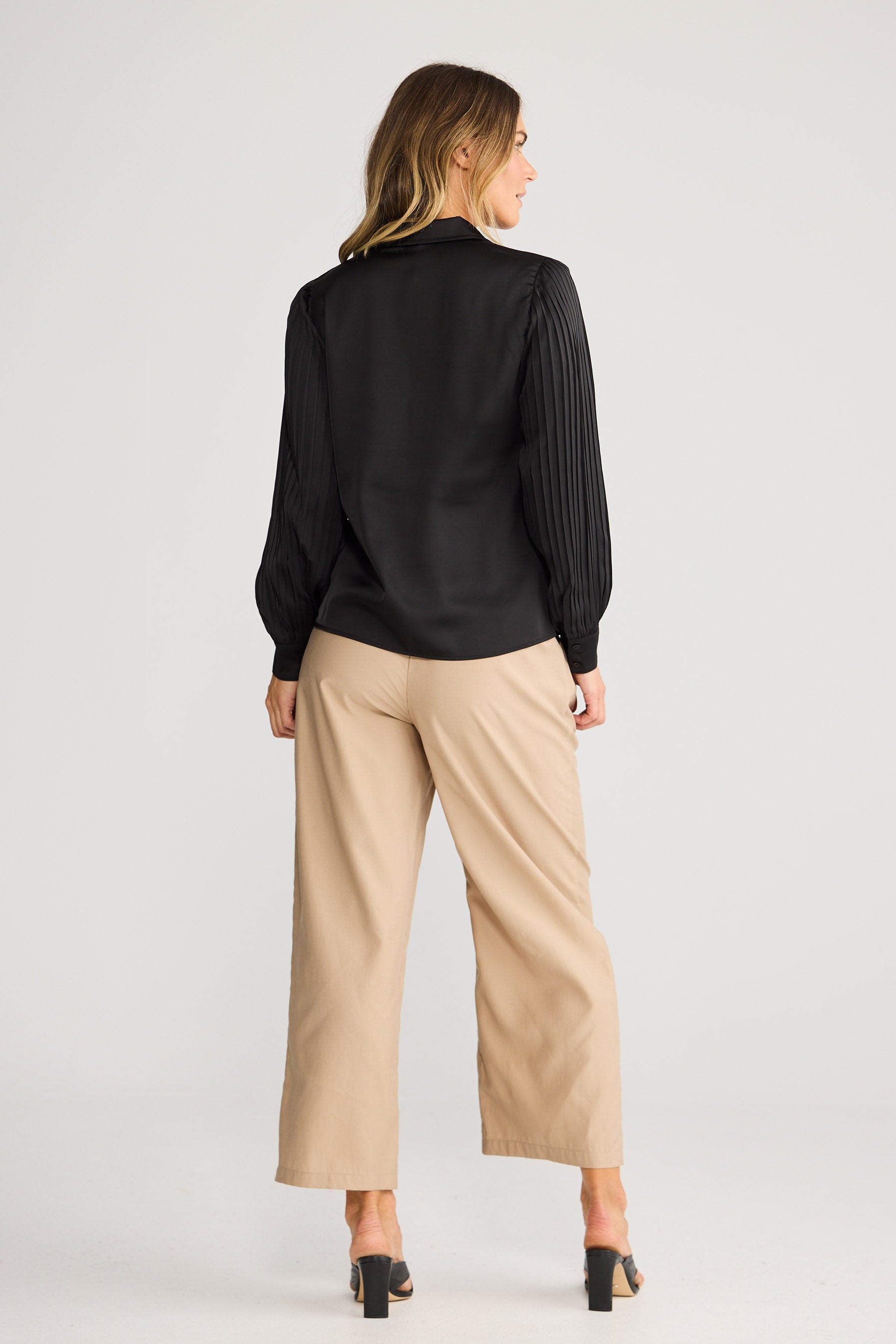 Woman wearing a black blouse and beige pants on a white background