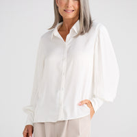 Woman wearing a white blouse and beige pants against a white background