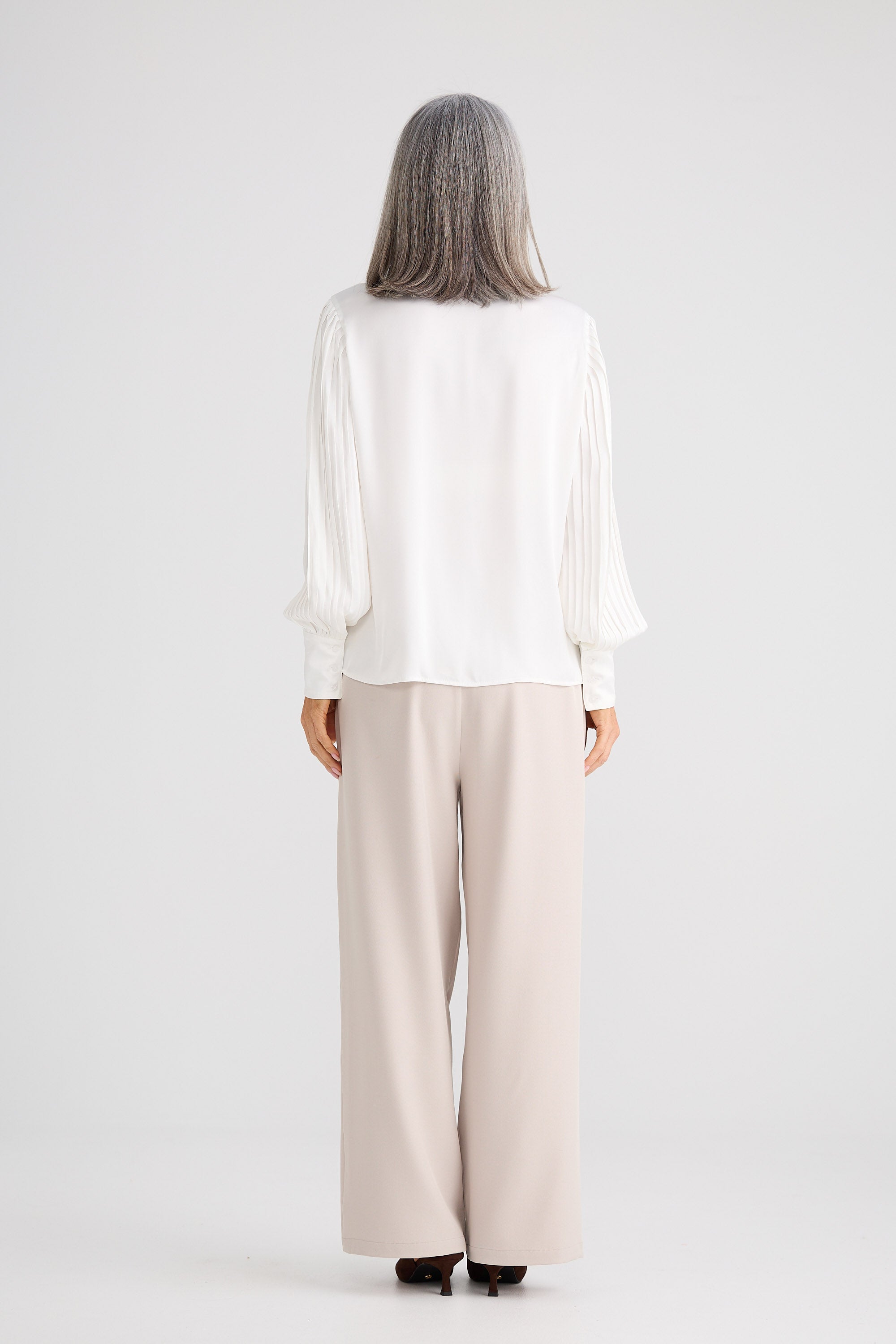 Person wearing a white blouse and beige pants on a white background