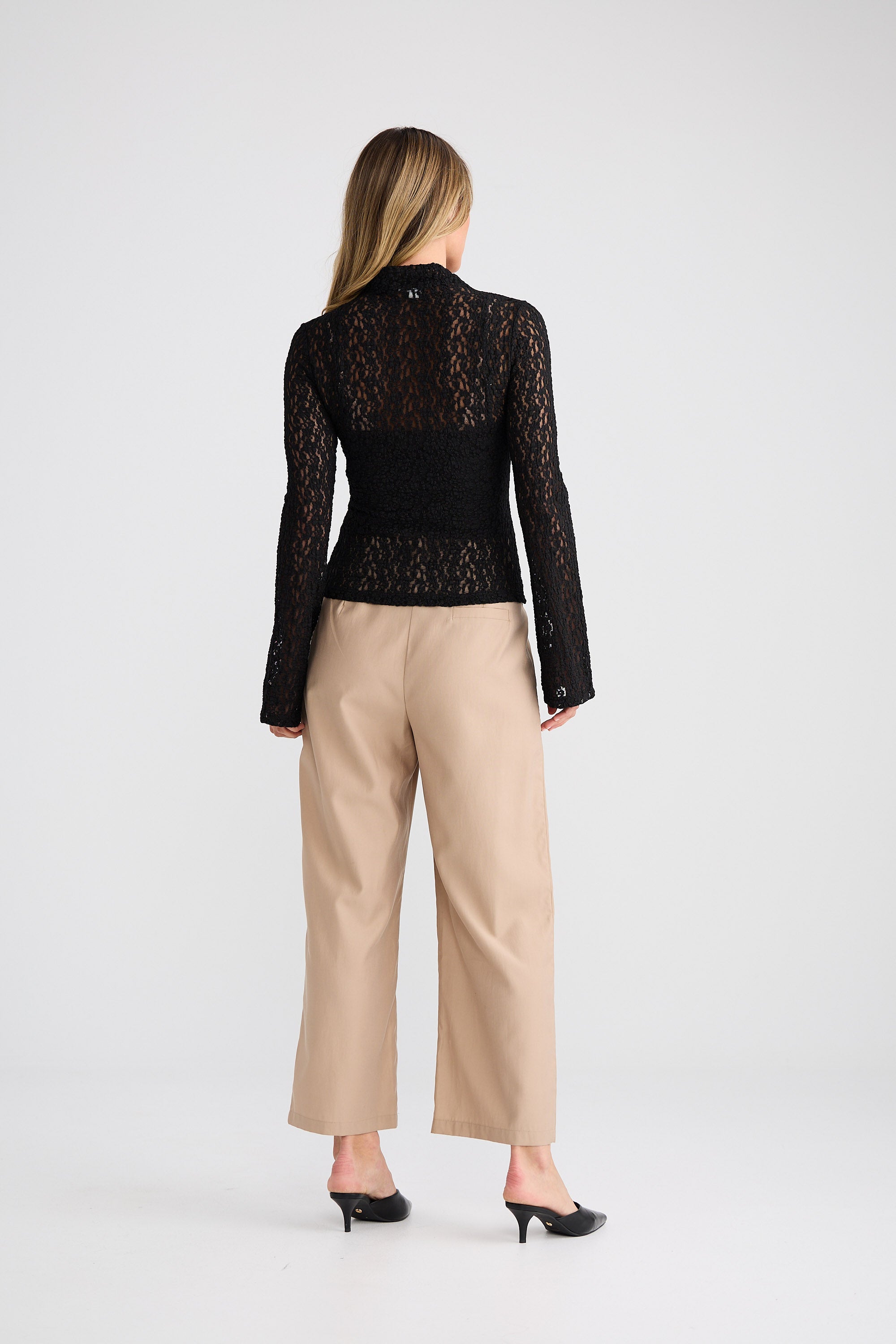 Woman wearing a black lace top and beige pants on a white background