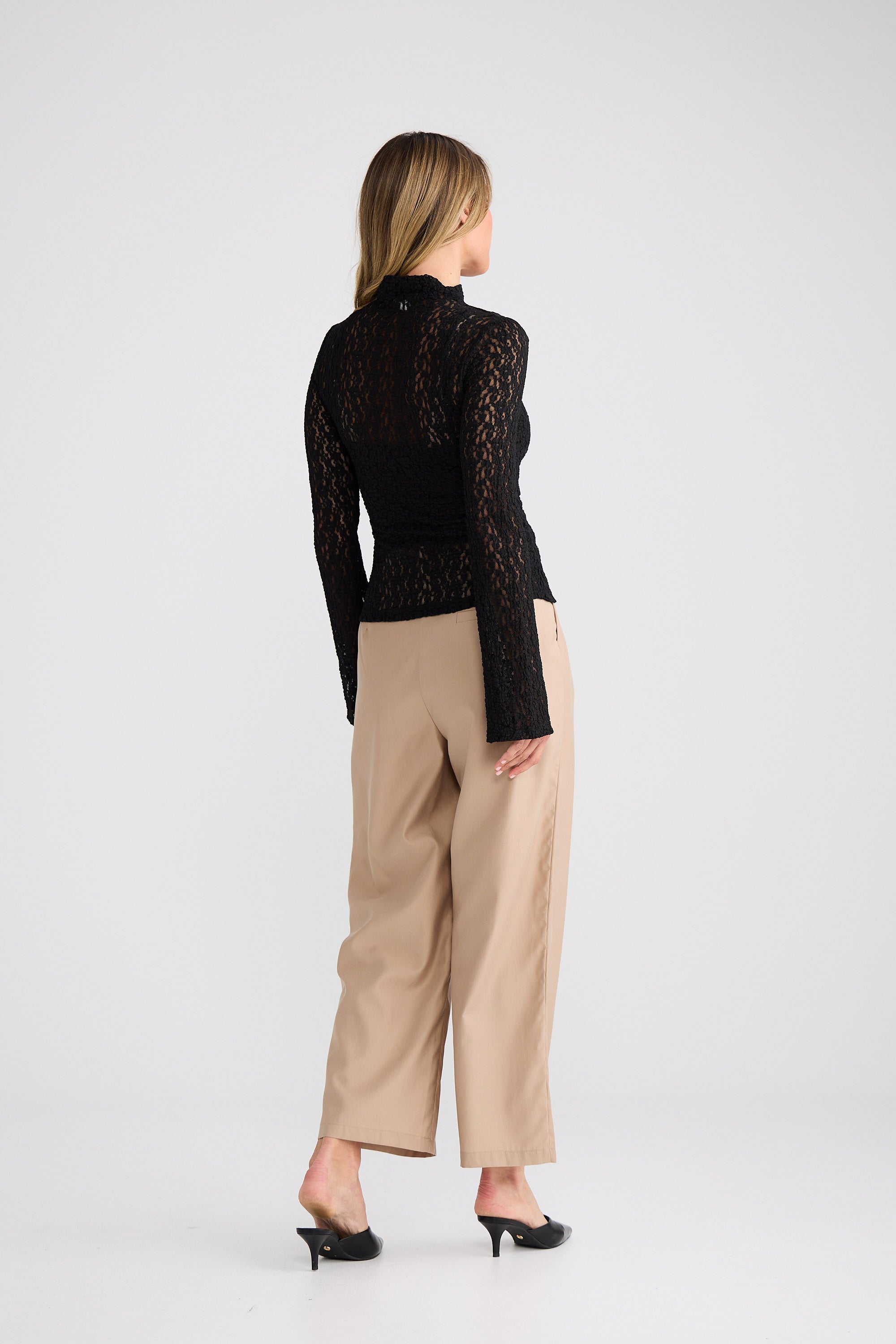 Woman wearing a black lace top and beige pants on a white background