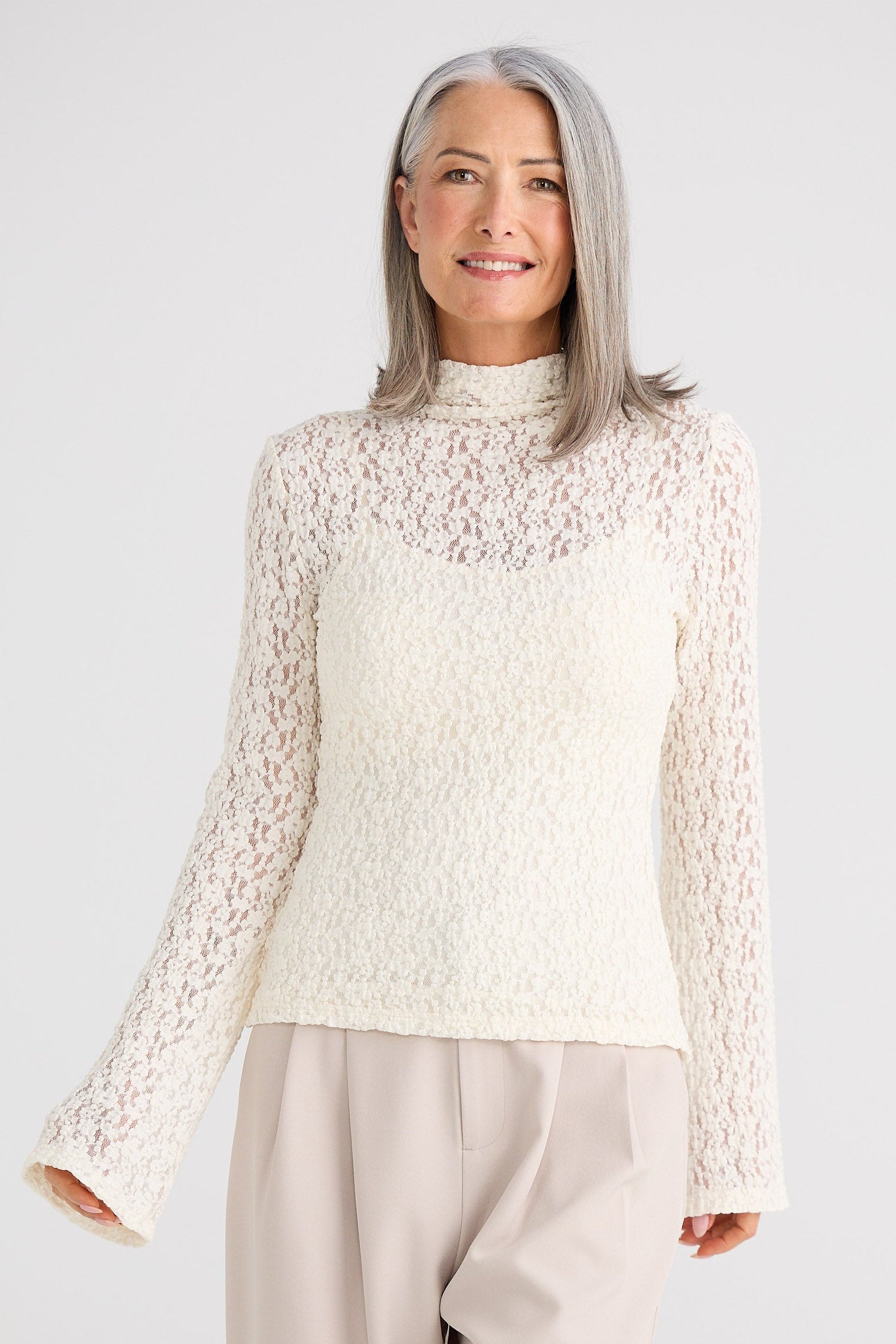 Woman wearing a white lace top and beige pants against a white background