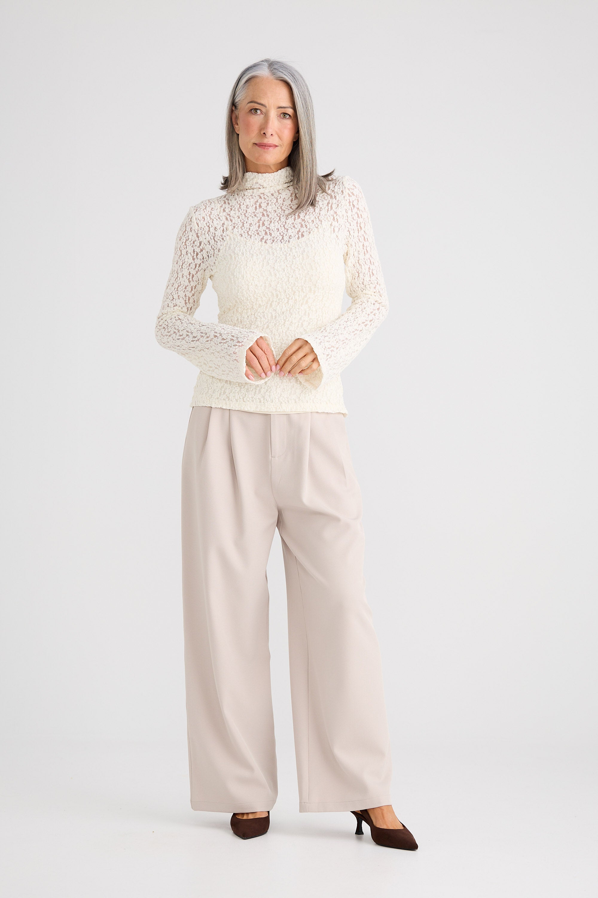 Woman wearing a white lace top and beige pants on a white background