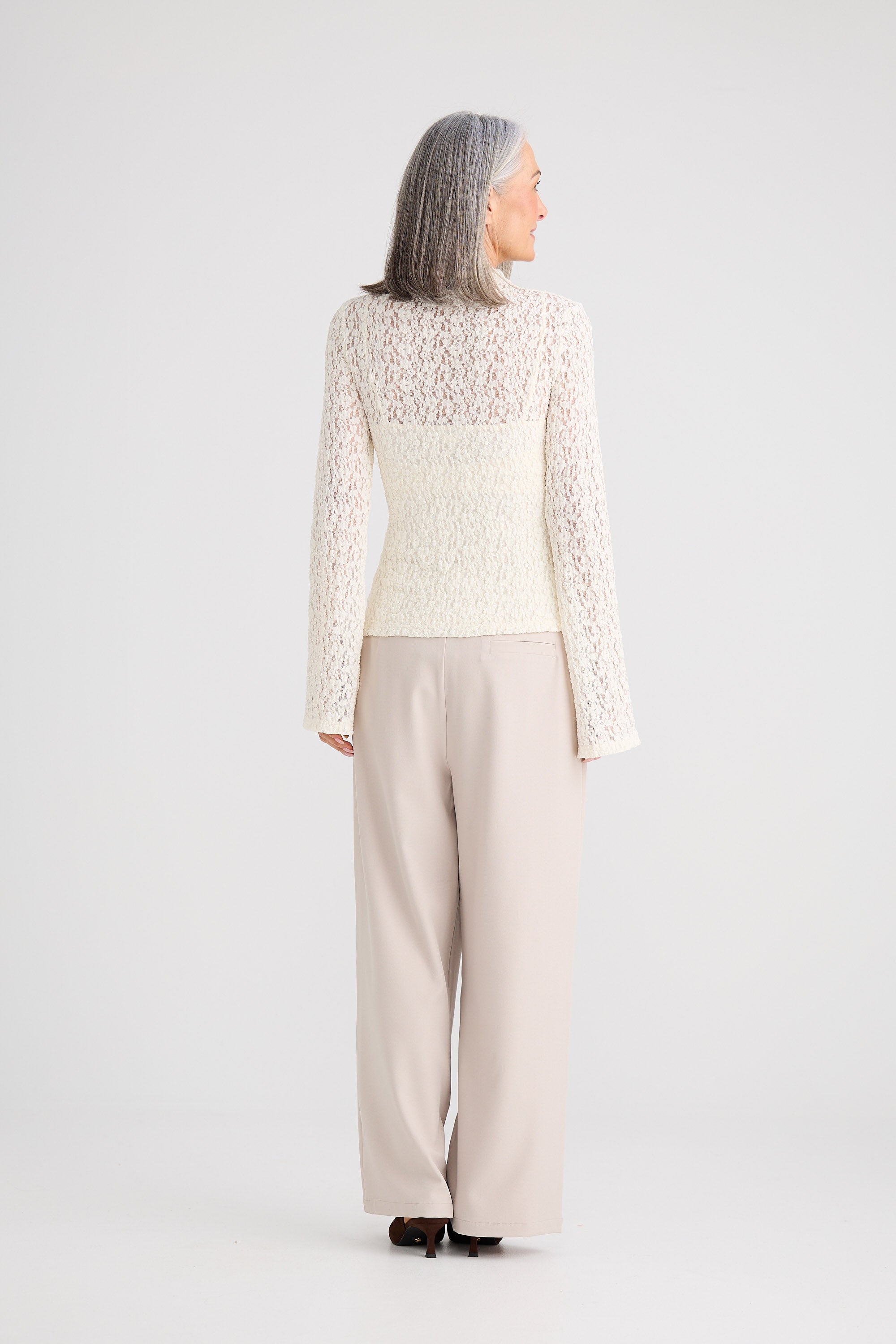Person wearing a light-colored lace top and beige pants on a white background