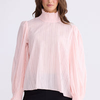 Model wearing Isolde Blouse in pink with high neck and bishop sleeves, front view on white background
