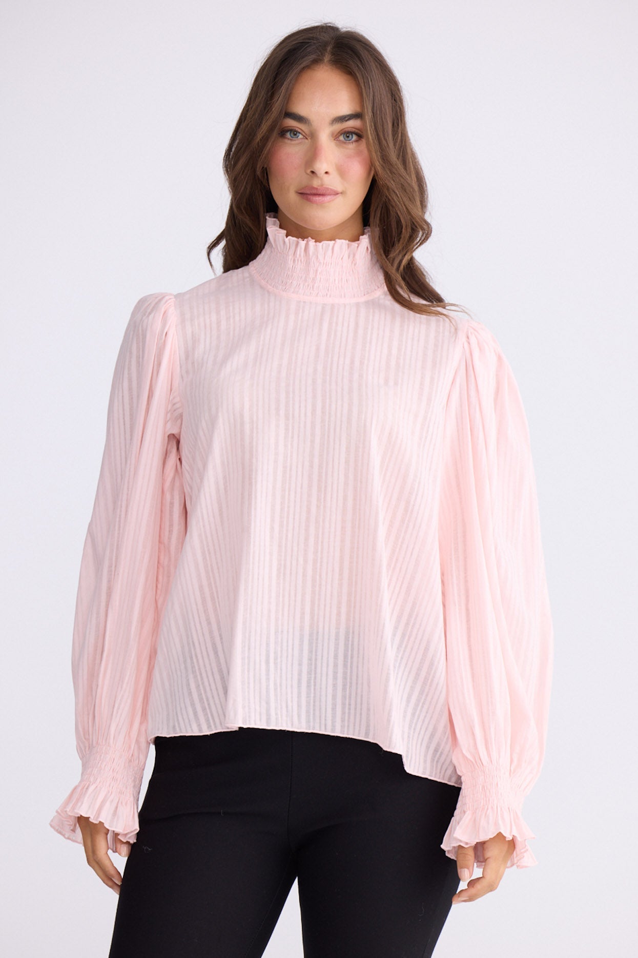 Model wearing Isolde Blouse in pink with high neck and bishop sleeves, front view on white background