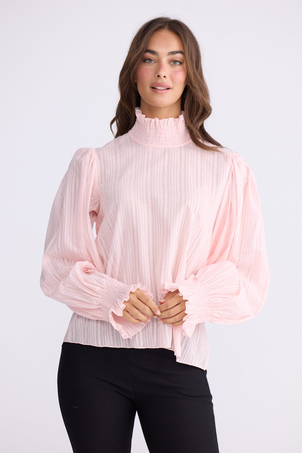 Model wearing Isolde Blouse in pink with high neck and bishop sleeves, front view on white background