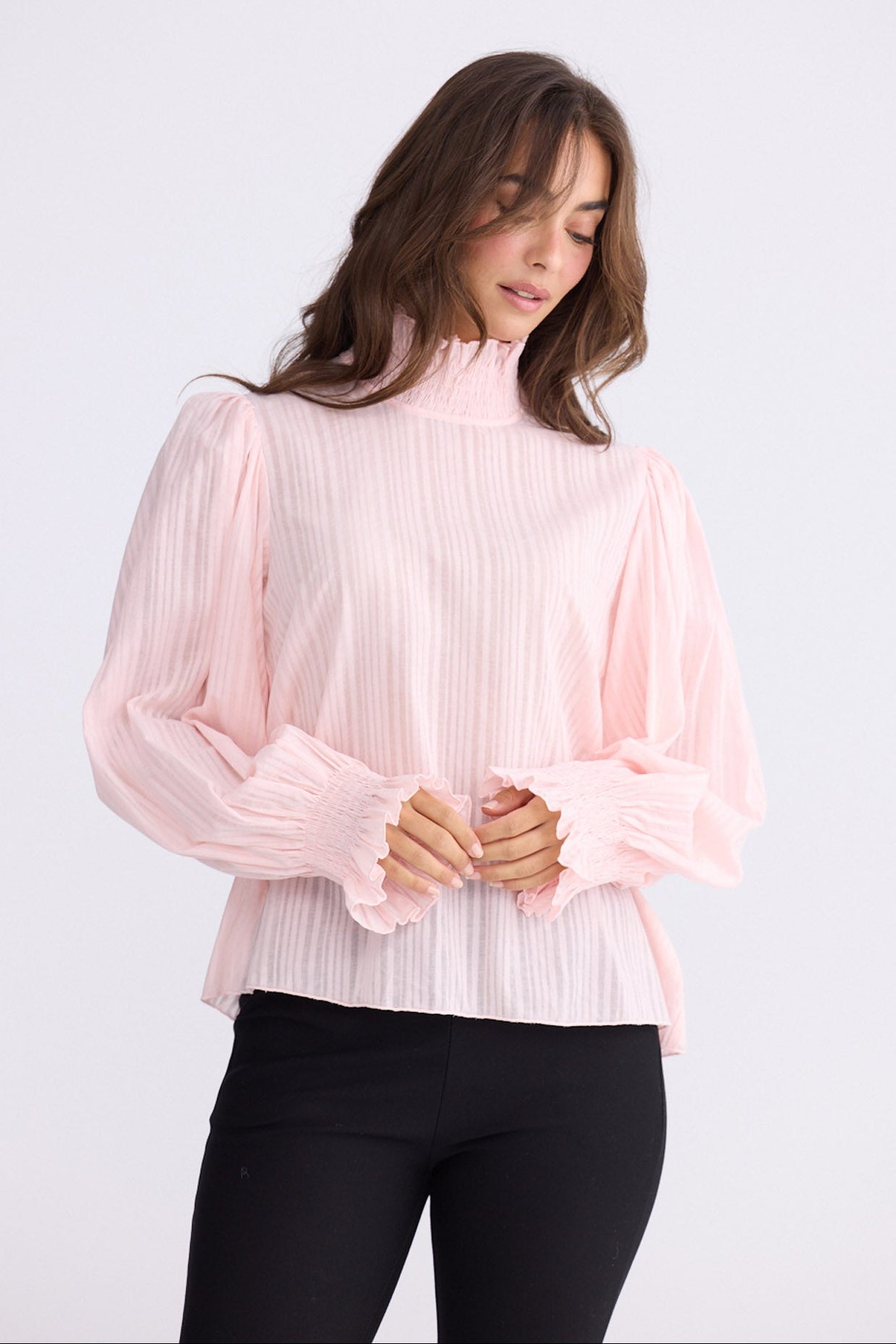 Model wearing Isolde Blouse in pink with high neck and bishop sleeves, front view on white background