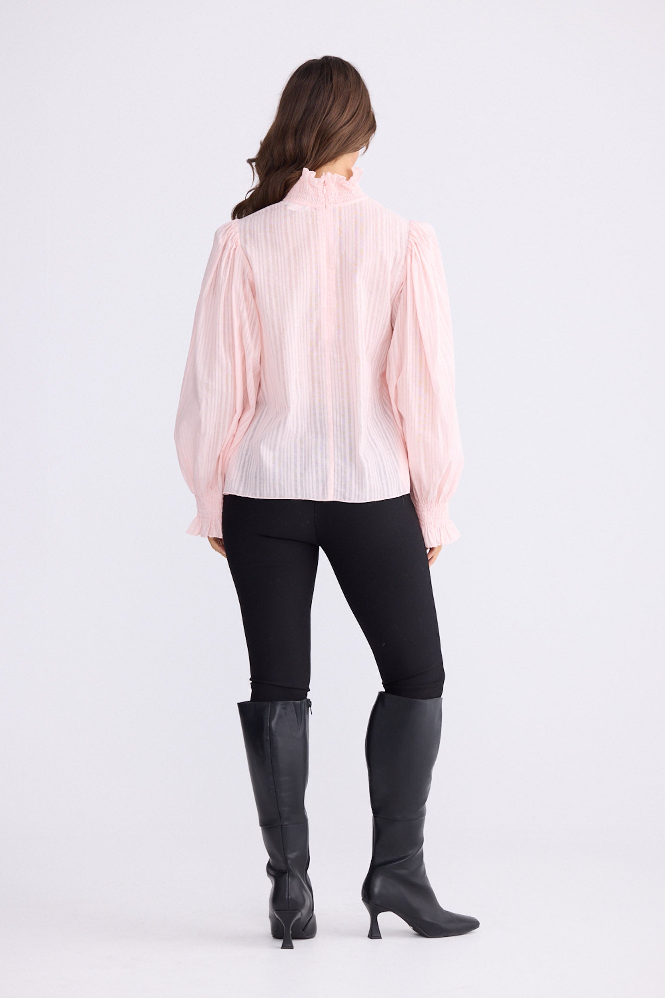 Model wearing Isolde Blouse in pink with high neck and bishop sleeves, back view on white background