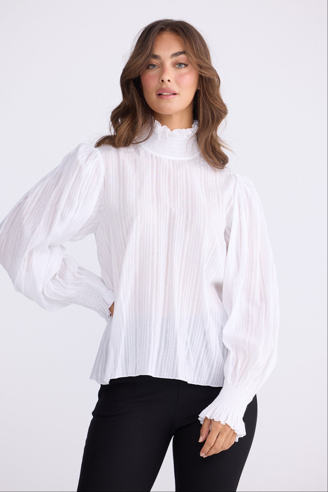 Model wearing Isolde Blouse in white with high neck and bishop sleeves, front view on white background
