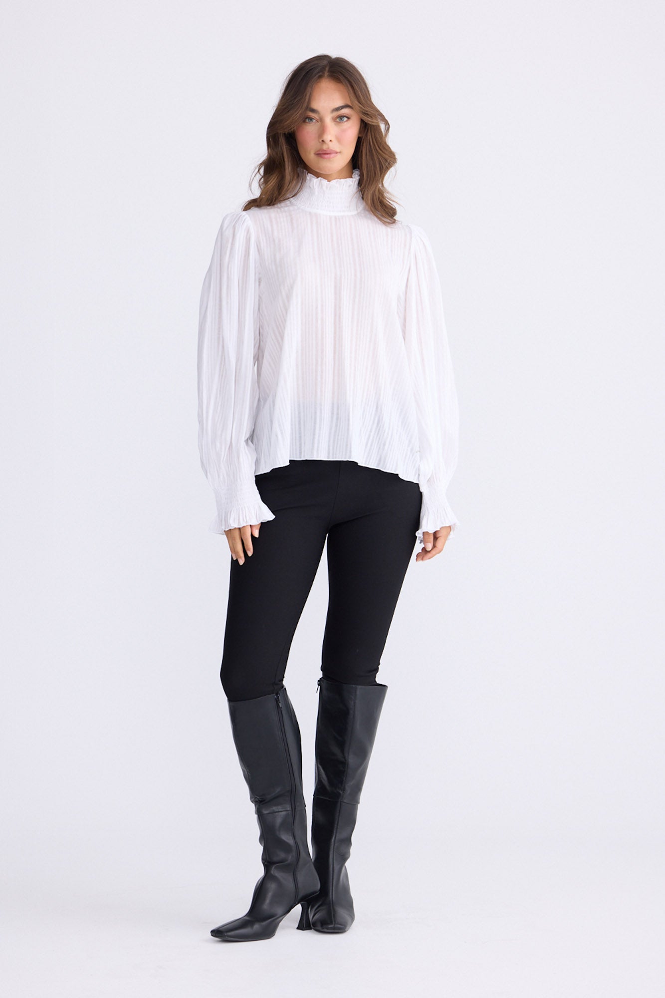 Model wearing Isolde Blouse in white with high neck and bishop sleeves, front view on white background