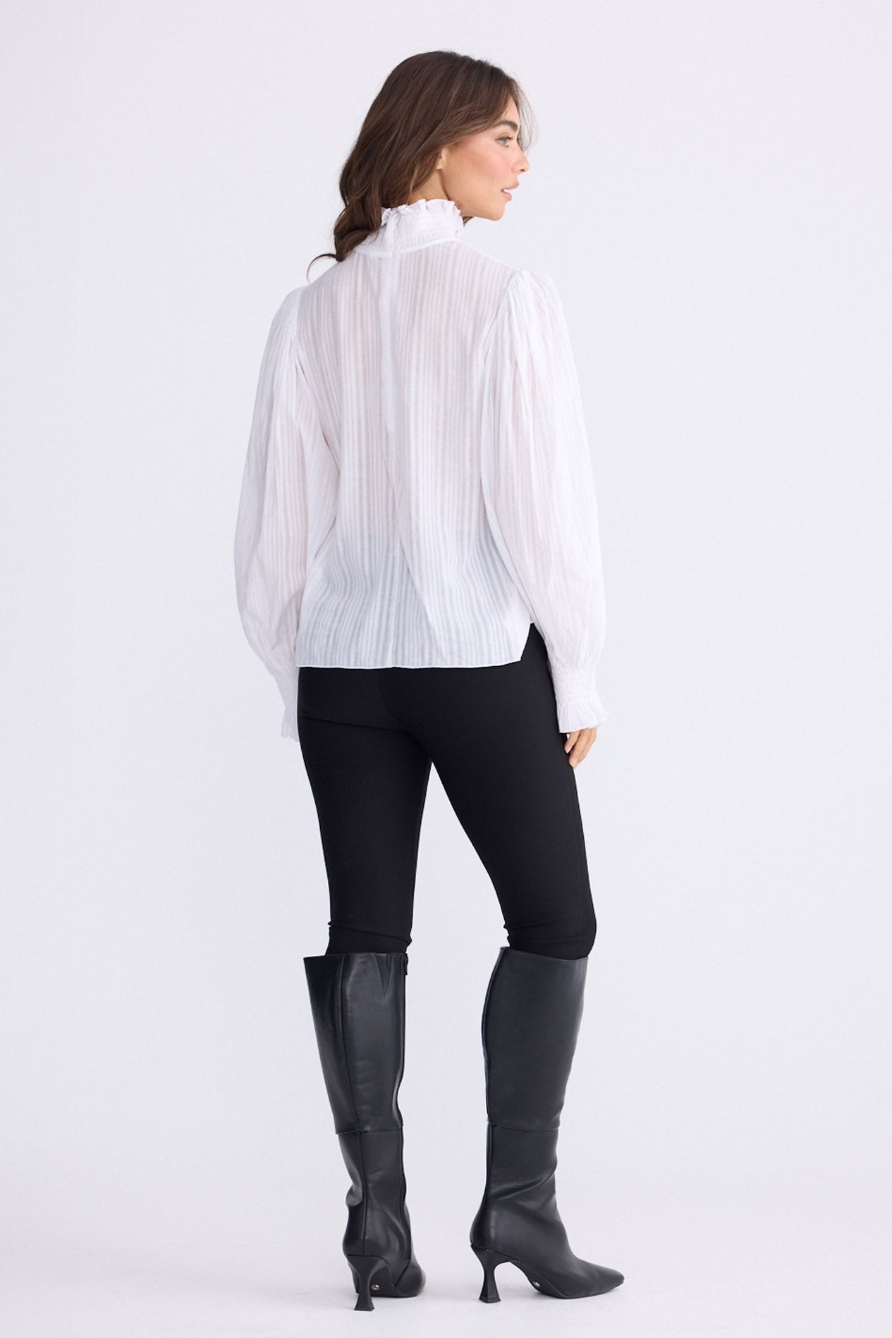 Model wearing Isolde Blouse in white with high neck and bishop sleeves, front view on white background