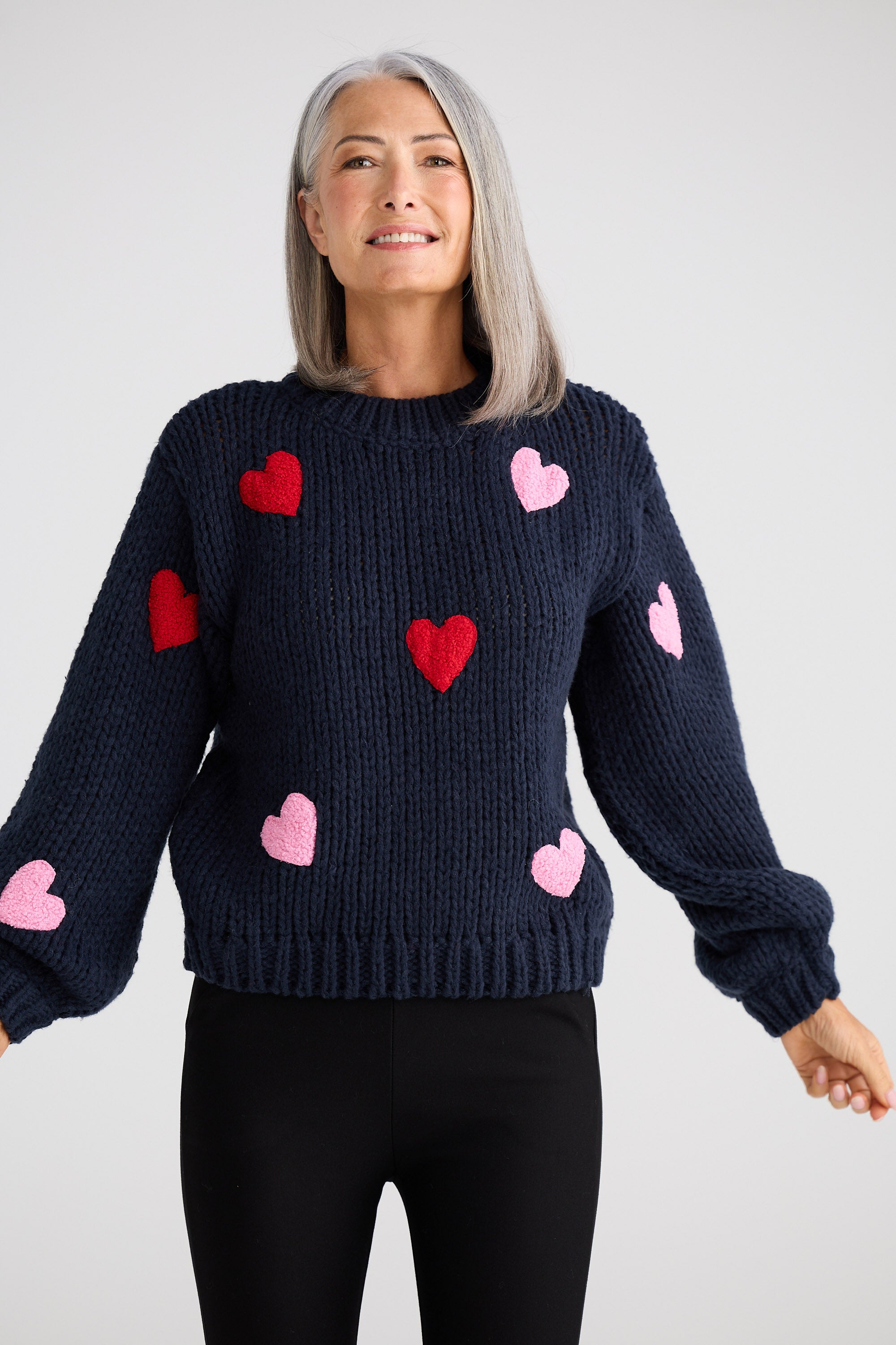 Woman wearing a navy blue sweater with red and pink heart patterns on a white background