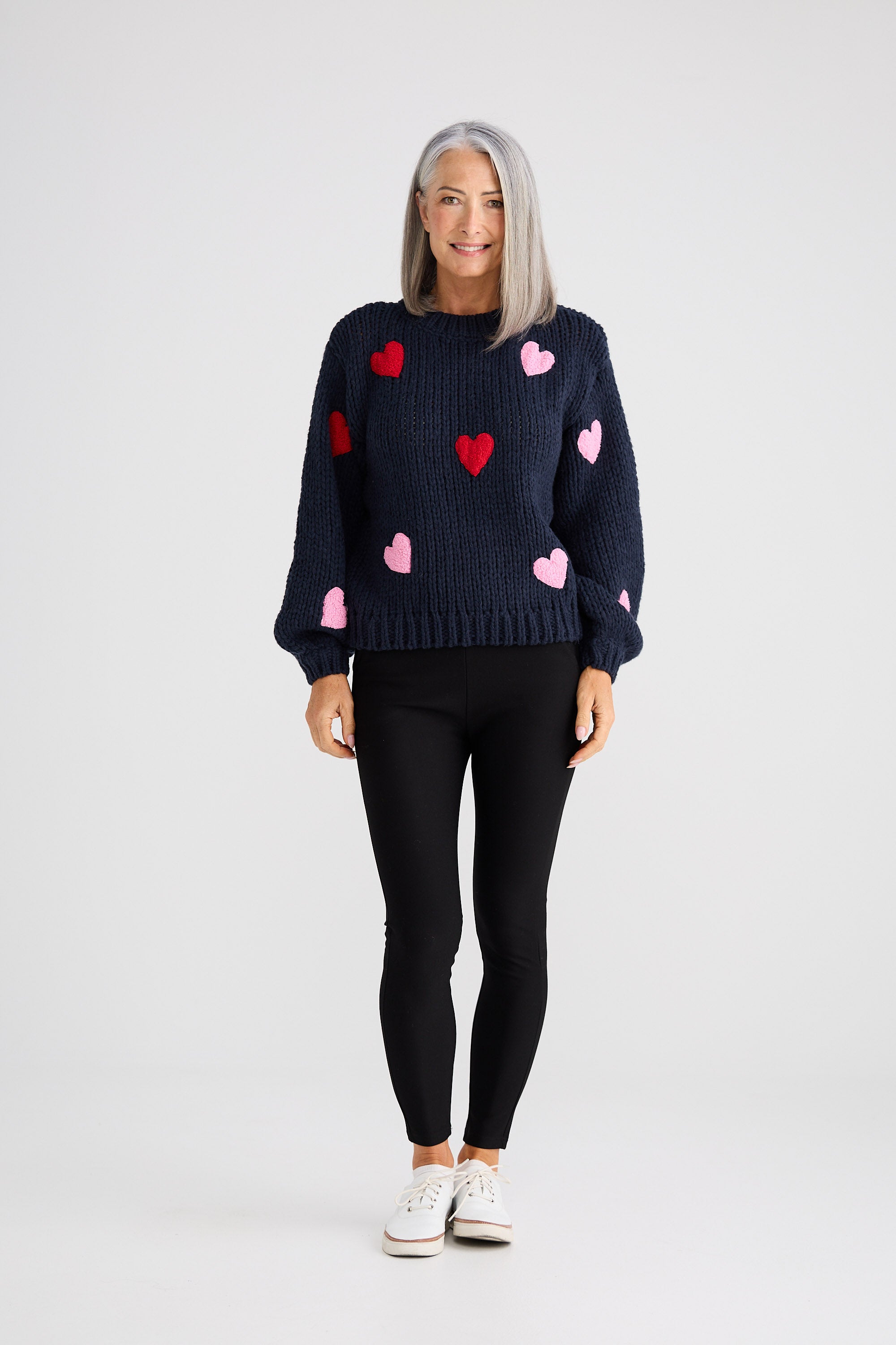 Woman wearing a navy sweater with pink and red heart patterns on a white background