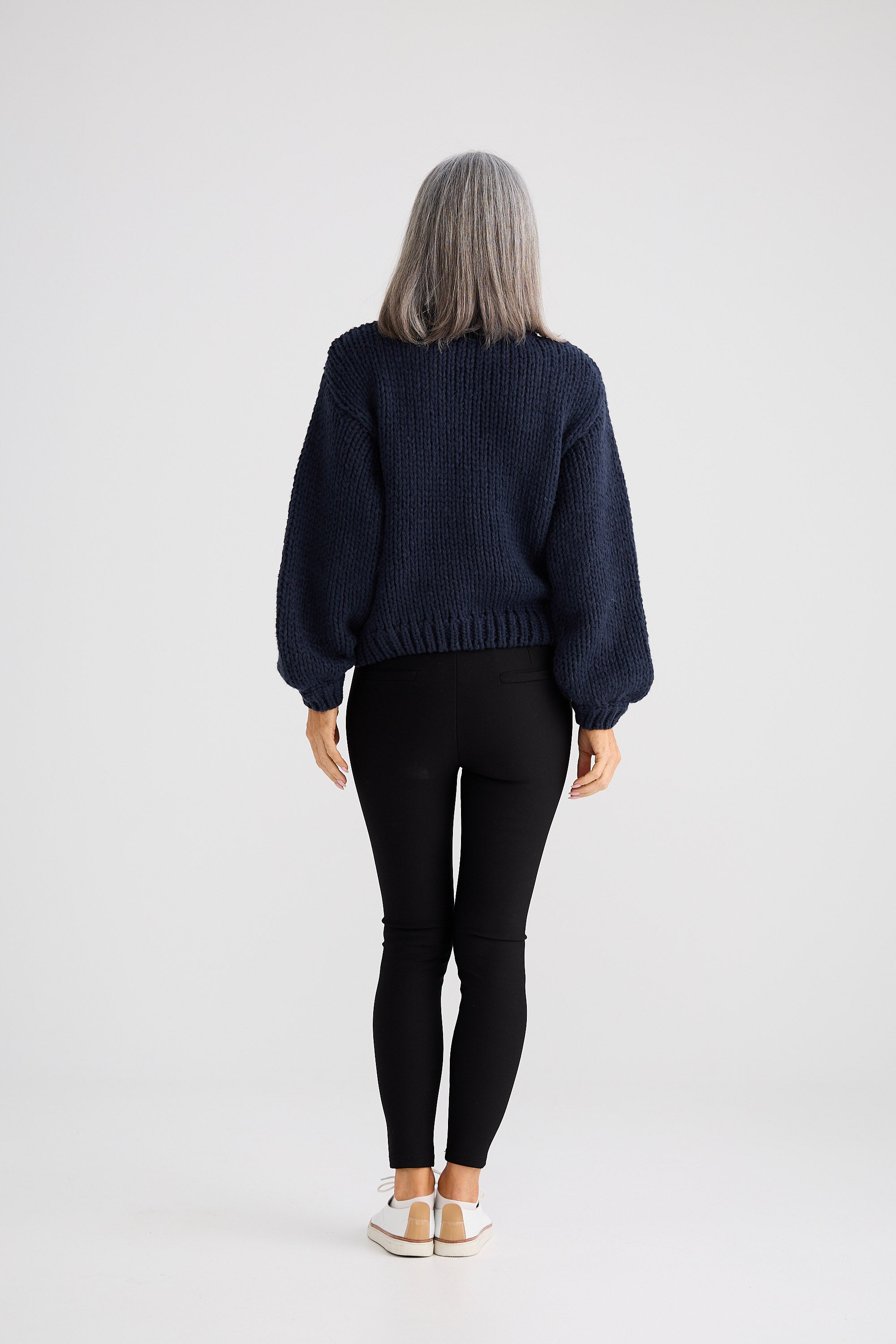 Person wearing a dark blue sweater and black pants on a white background