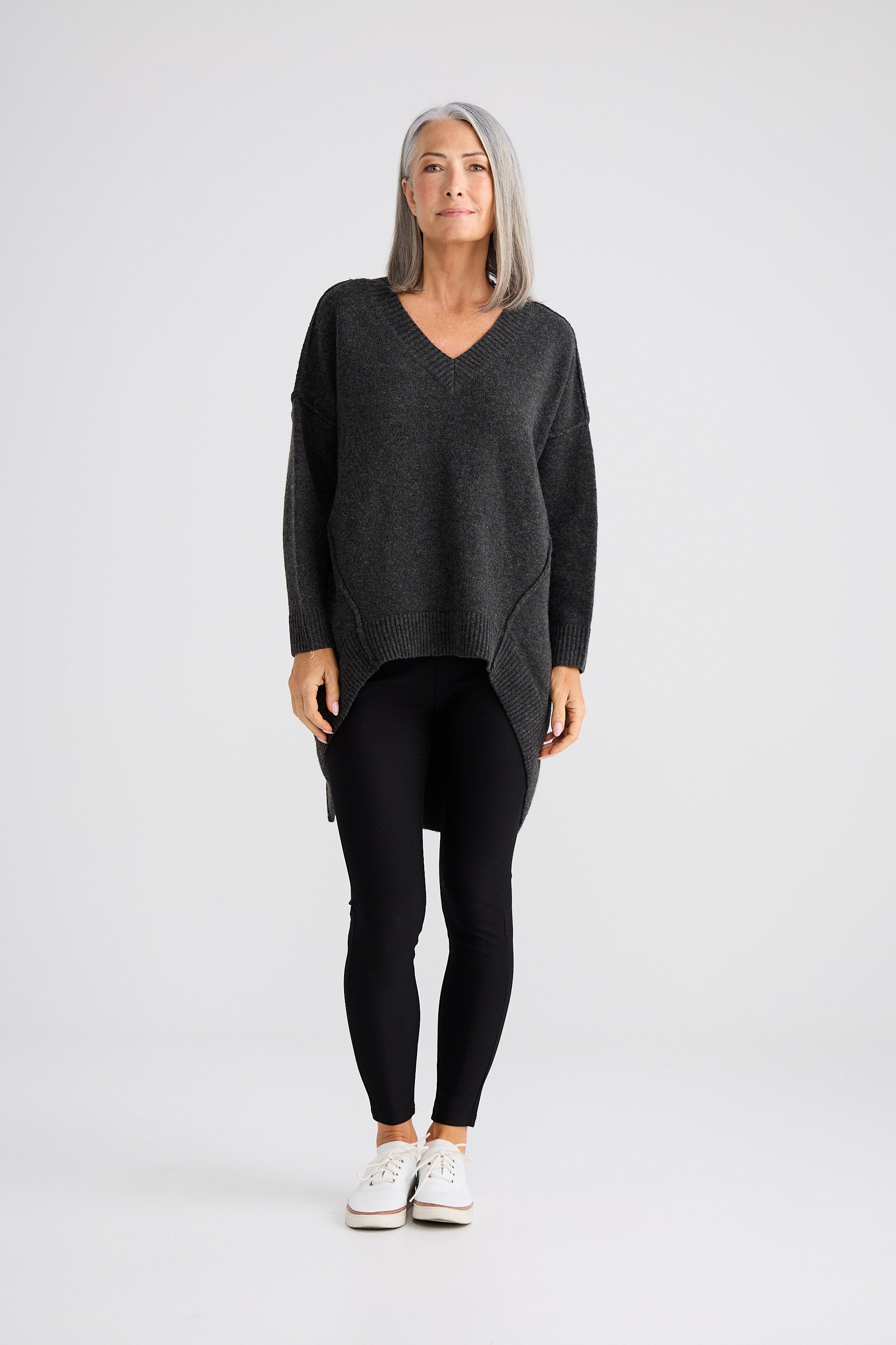 Woman wearing a dark gray sweater and black leggings on a white background