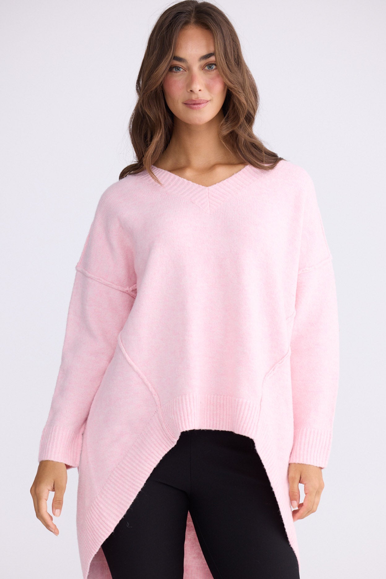 Model wearing Wiltshire soft pink knit sweater with V-neck and high-low hem, front view on white background