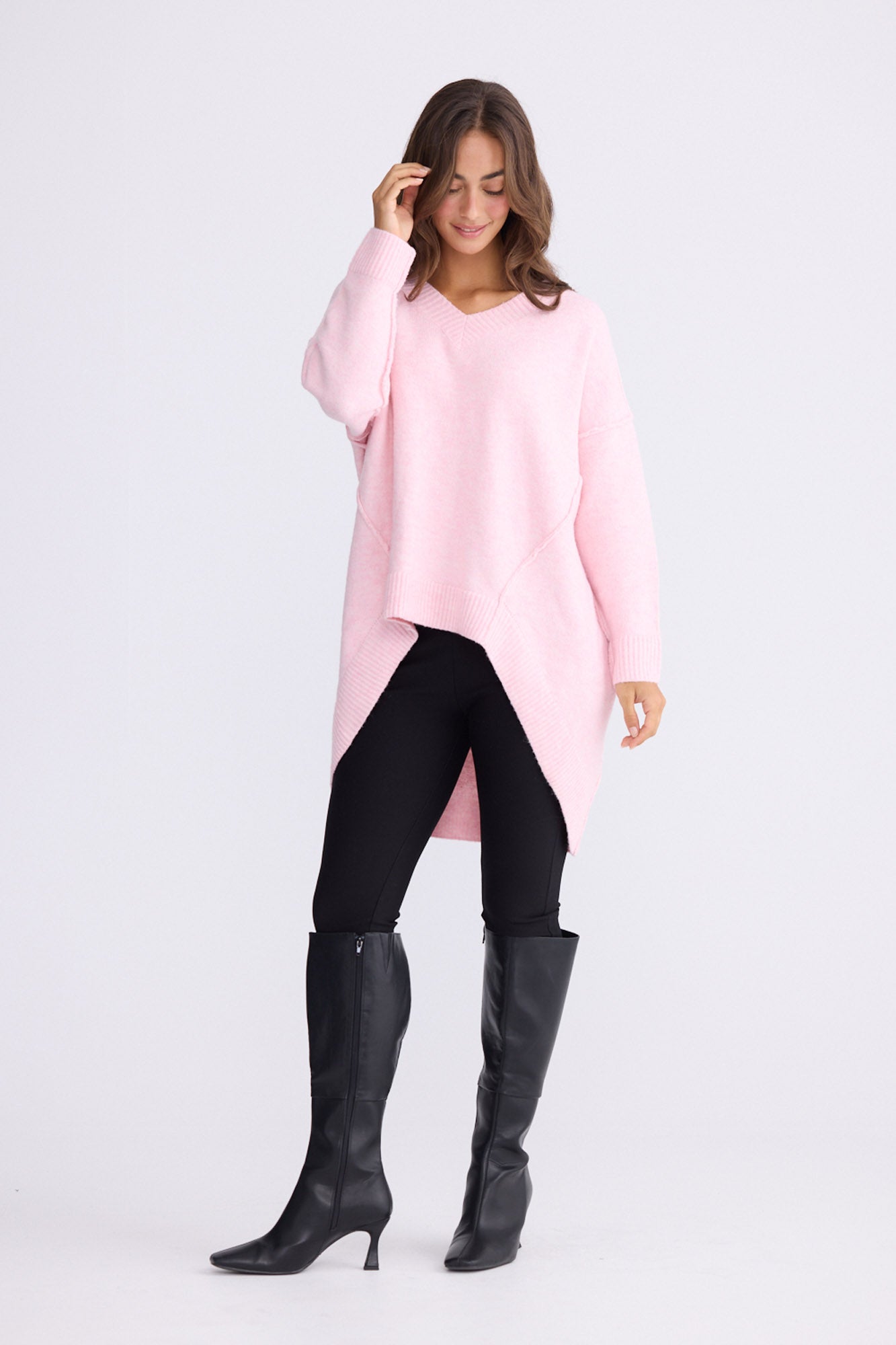 Model wearing Wiltshire soft pink knit sweater with V-neck and high-low hem, alternate view on white background