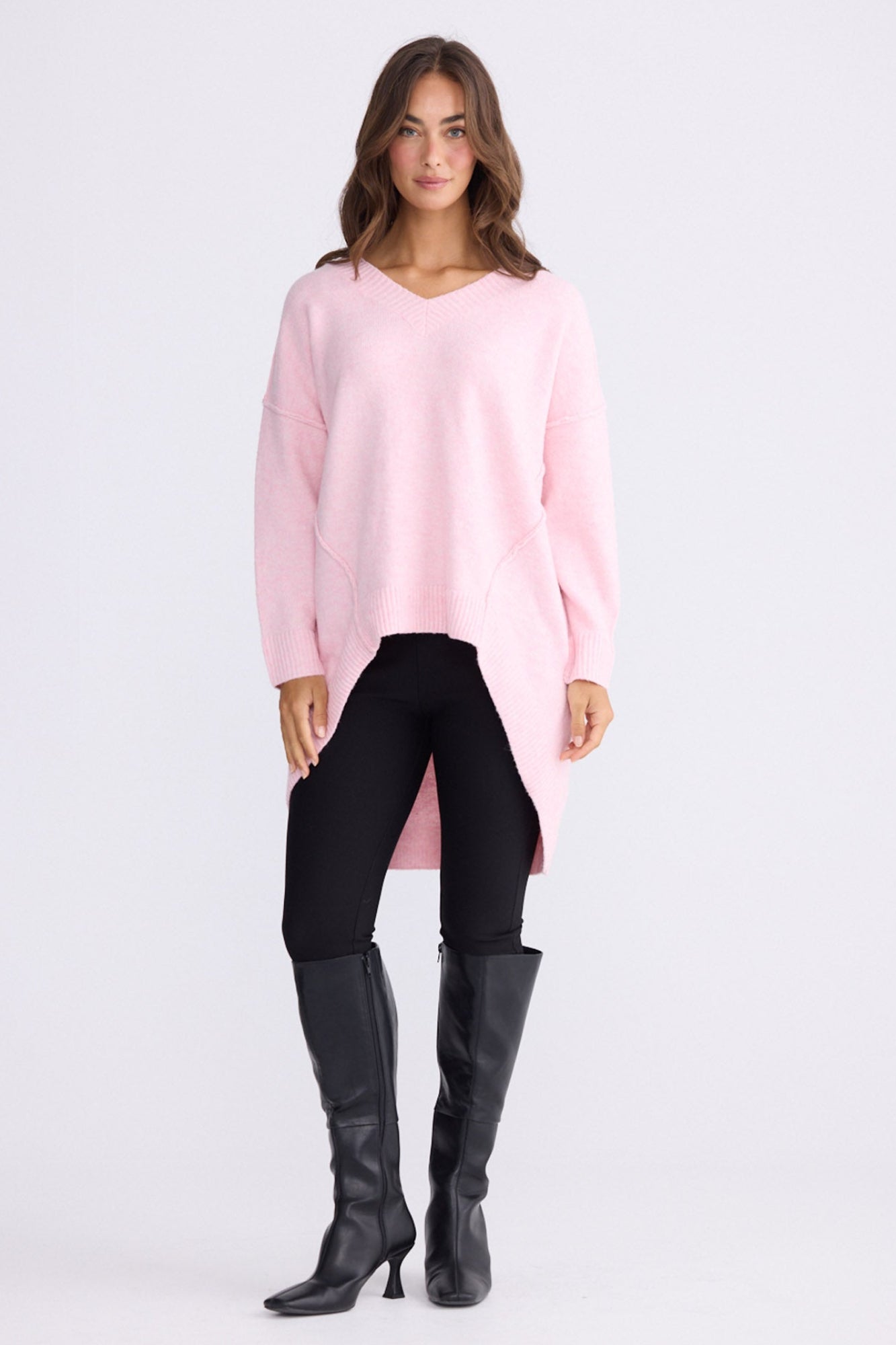 Model wearing Wiltshire soft pink knit sweater with V-neck and high-low hem, alternate view on white background