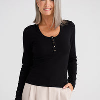 Woman wearing a black long-sleeve top and beige pants on a white background
