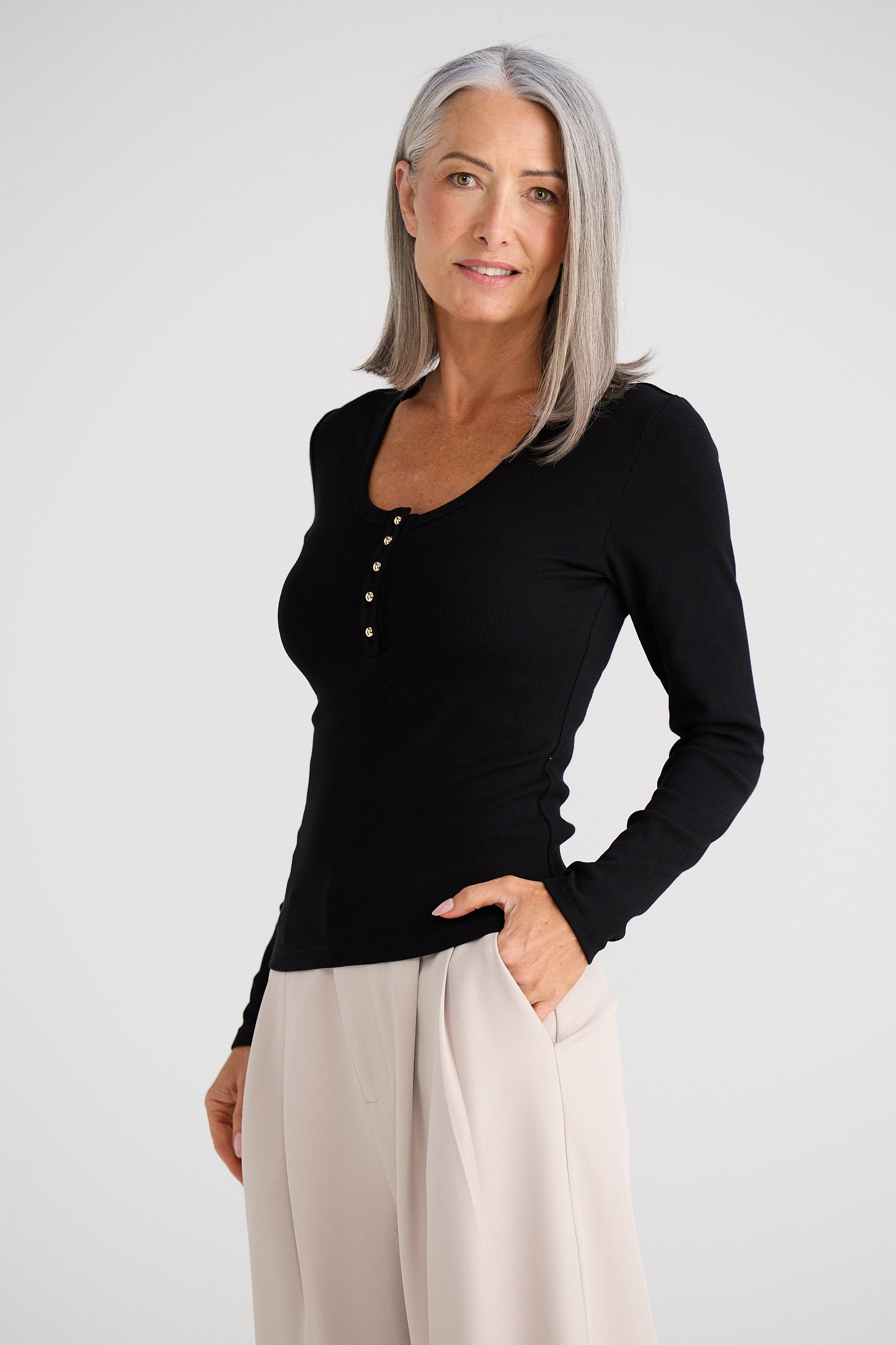Woman wearing a black long-sleeve top and beige pants on a white background
