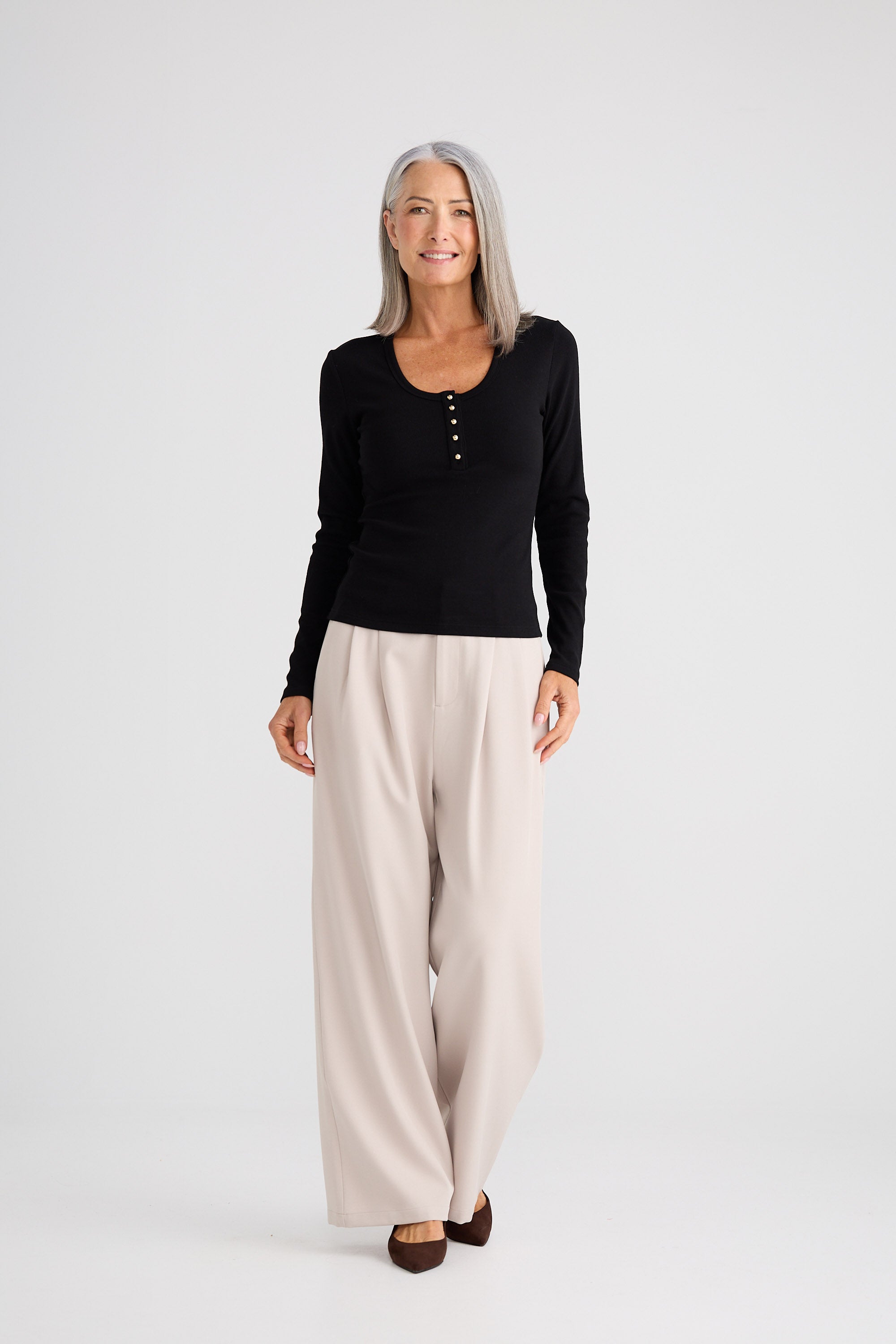 Woman wearing a black long-sleeve top and beige wide-leg pants on a white background