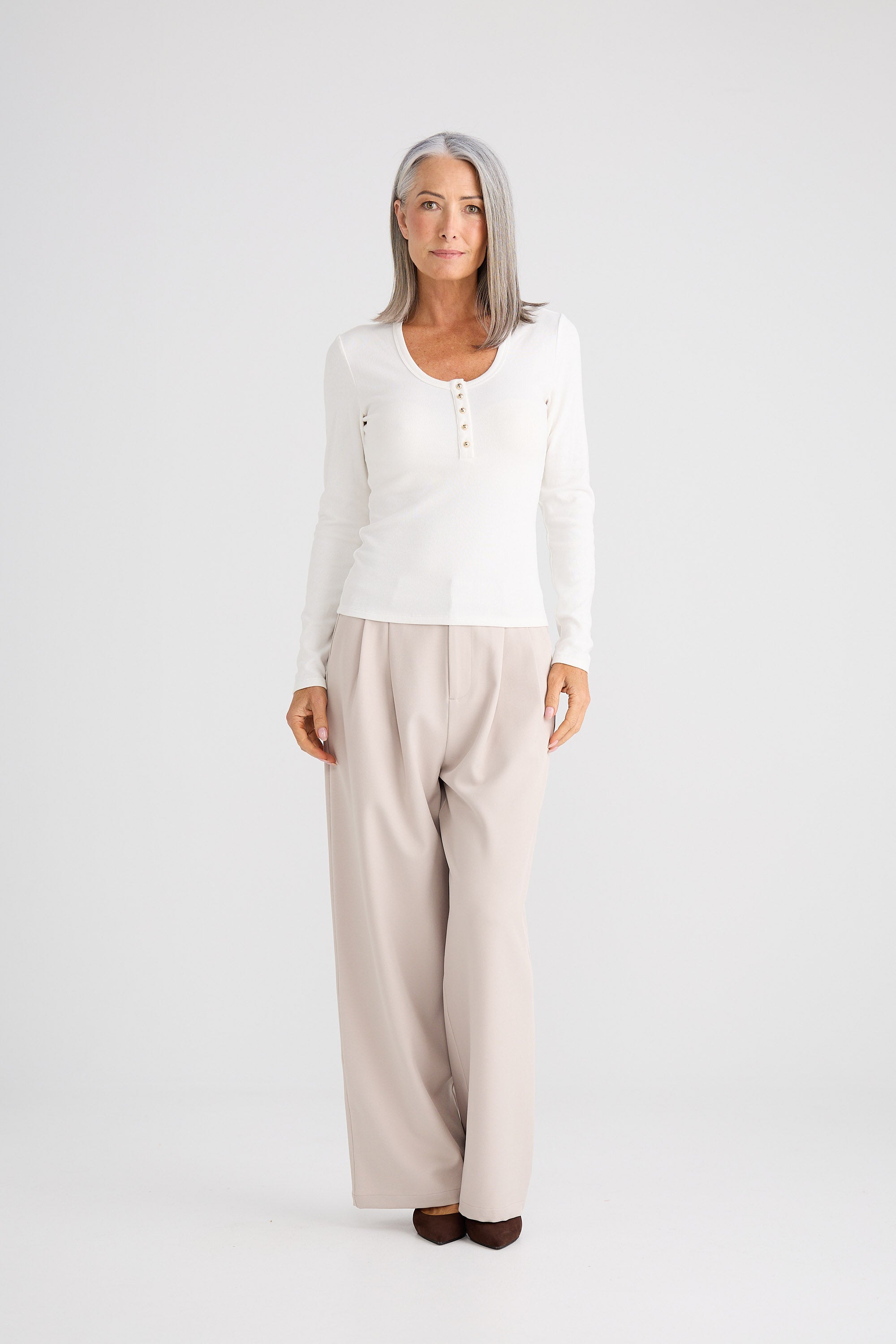 Woman wearing a white long-sleeve top and beige pants on a white background