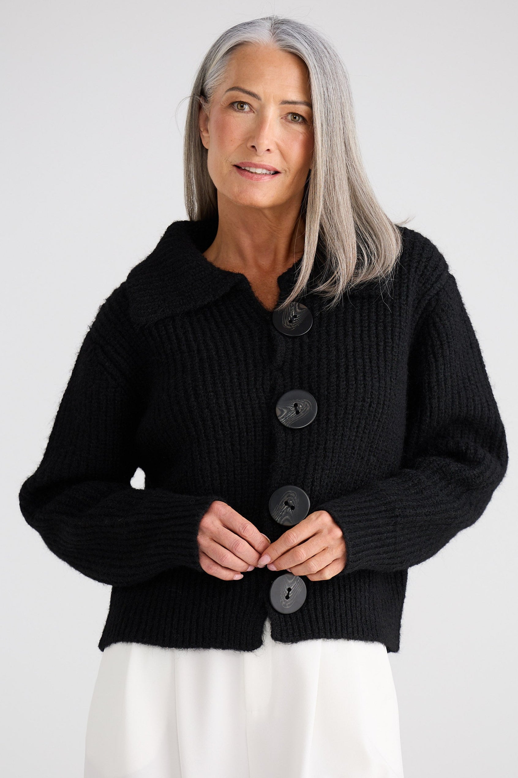 Woman wearing a black knitted cardigan with buttons on a white background