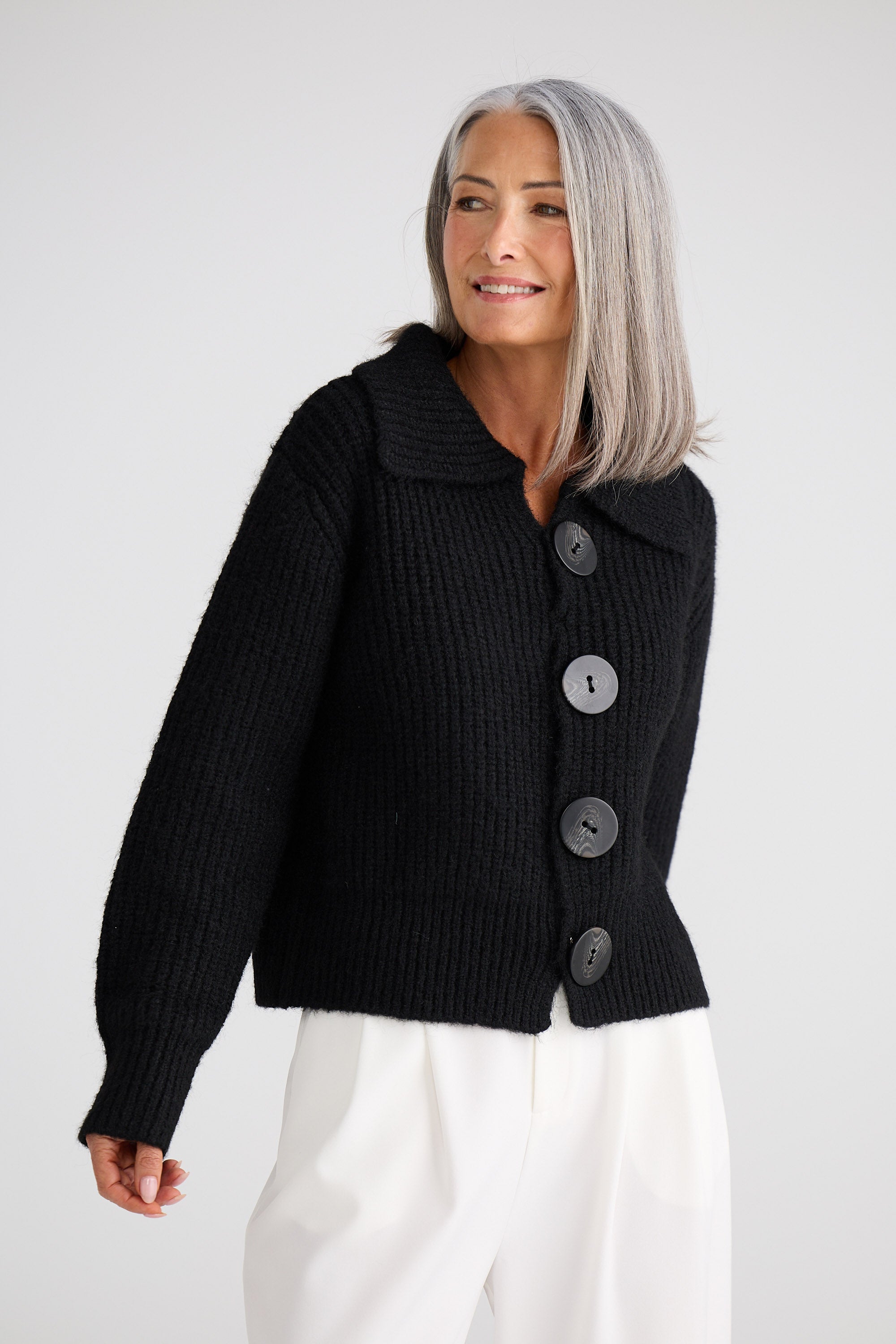 Woman wearing a black ribbed knit cardigan with buttons on a white background