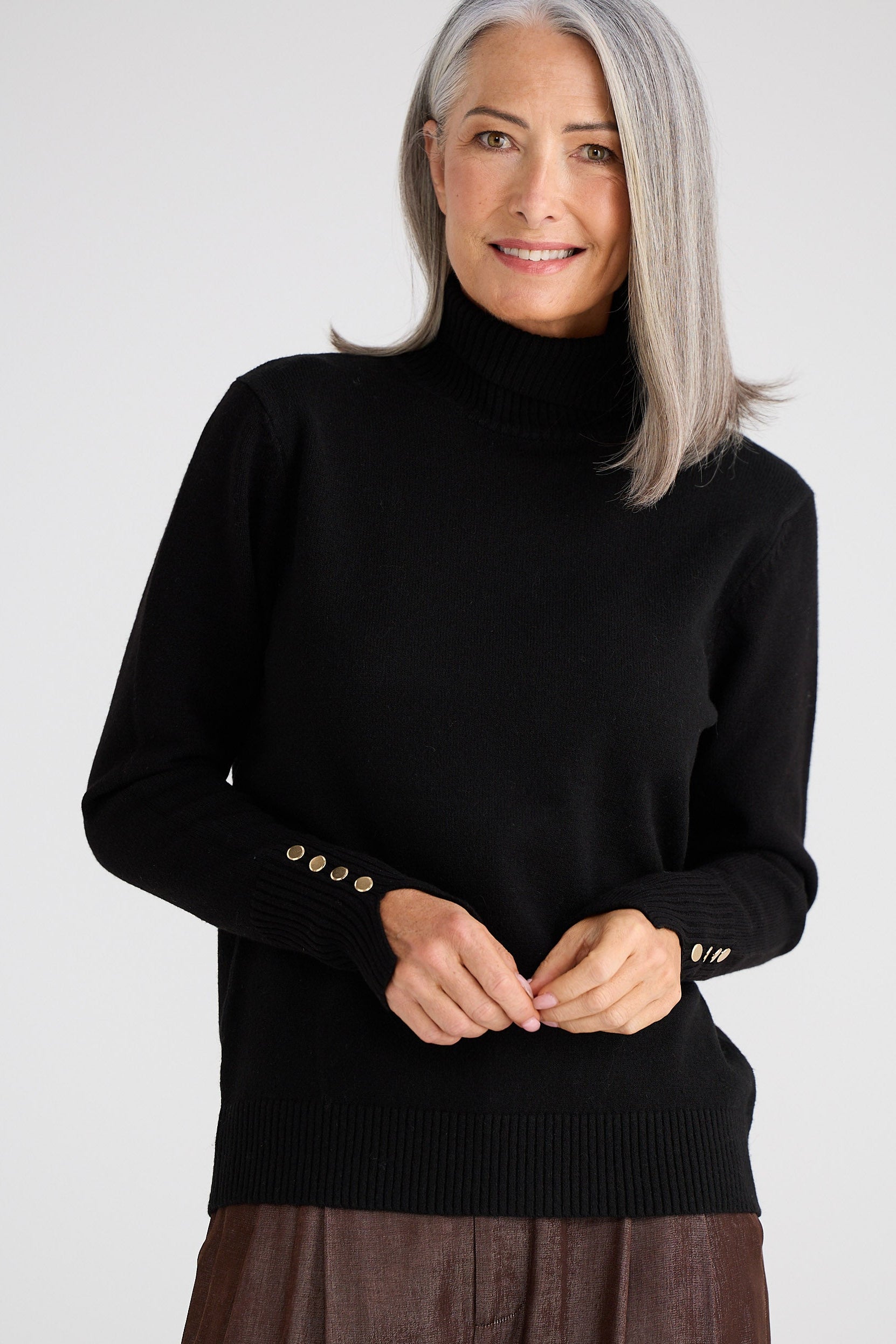 Woman wearing a black turtleneck sweater with gold buttons on a white background