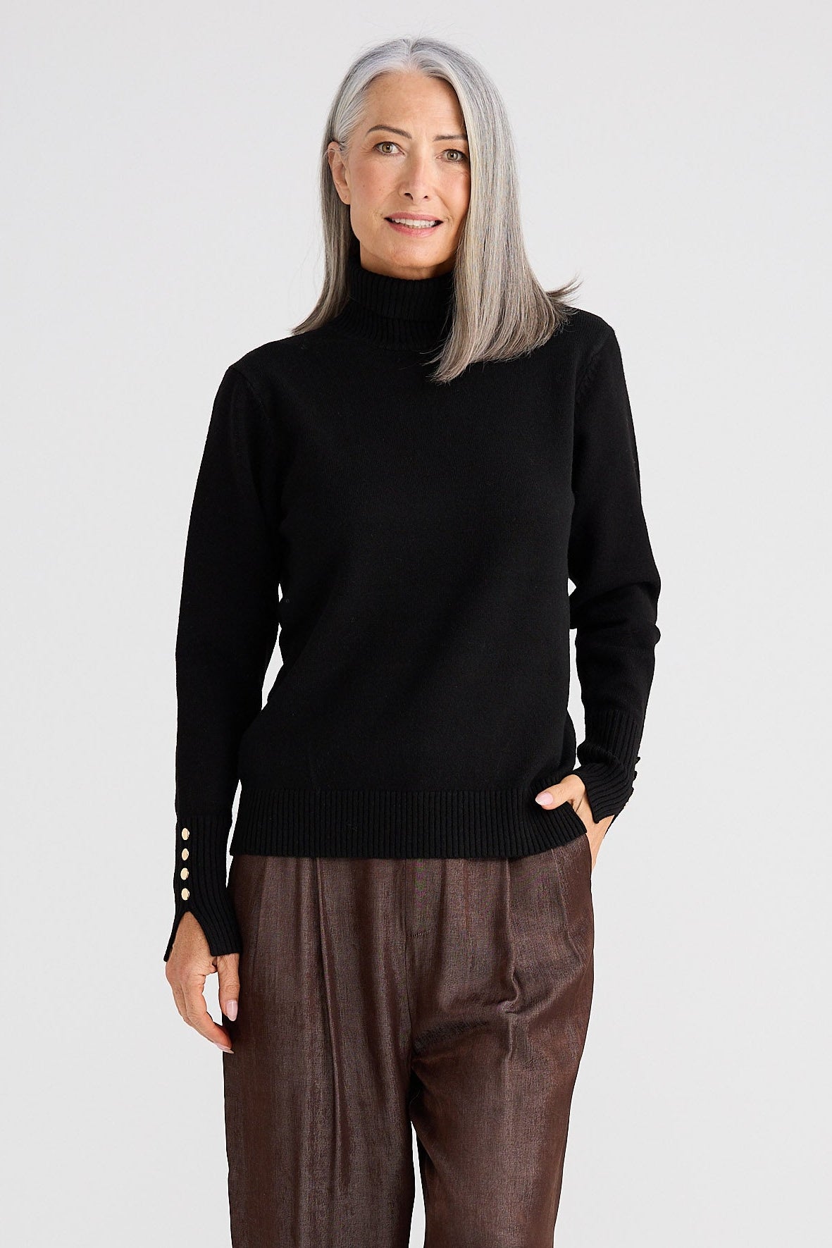 Woman wearing a black turtleneck and brown pants on a white background