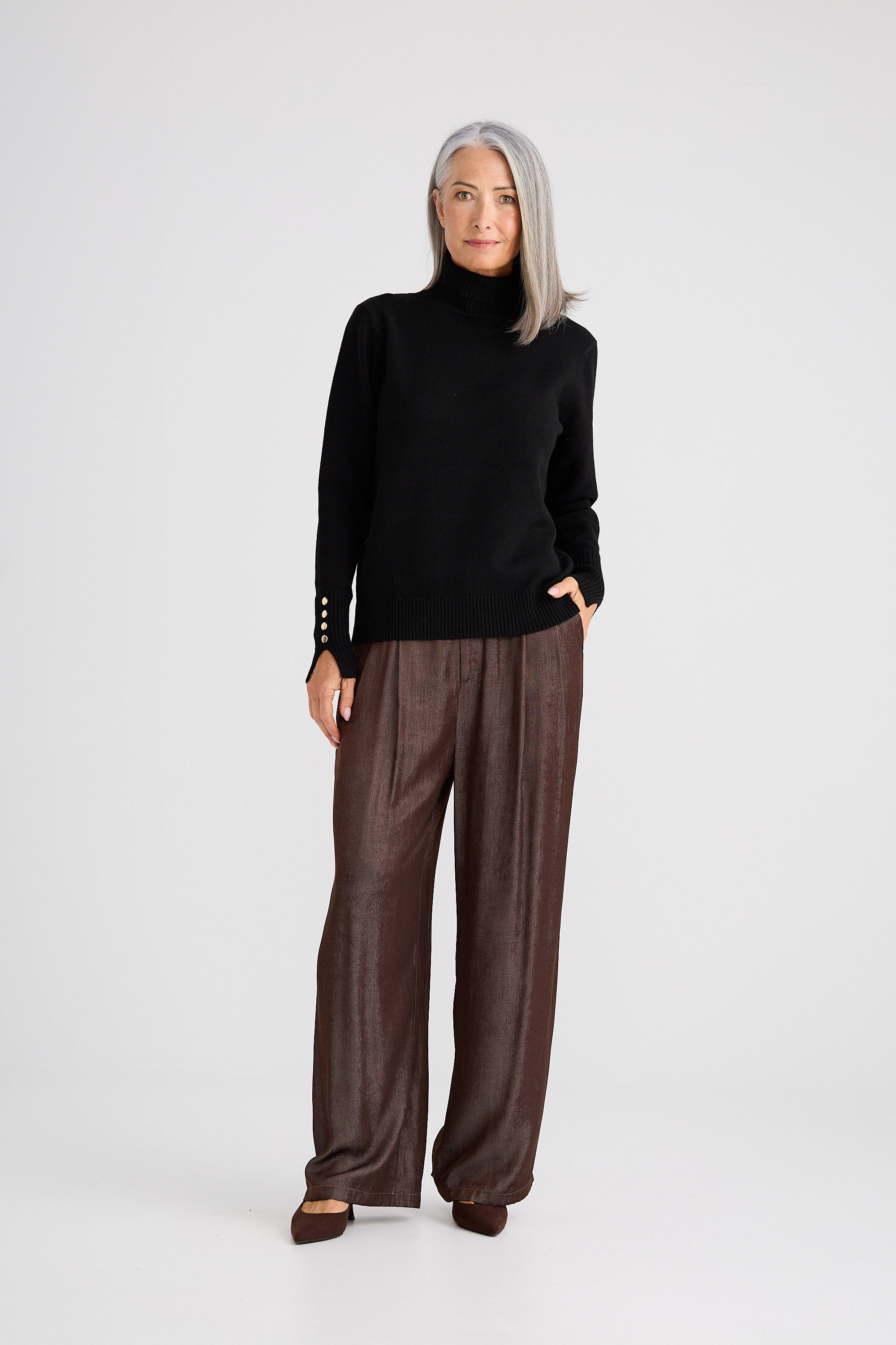 Woman wearing a black turtleneck and brown pants on a white background