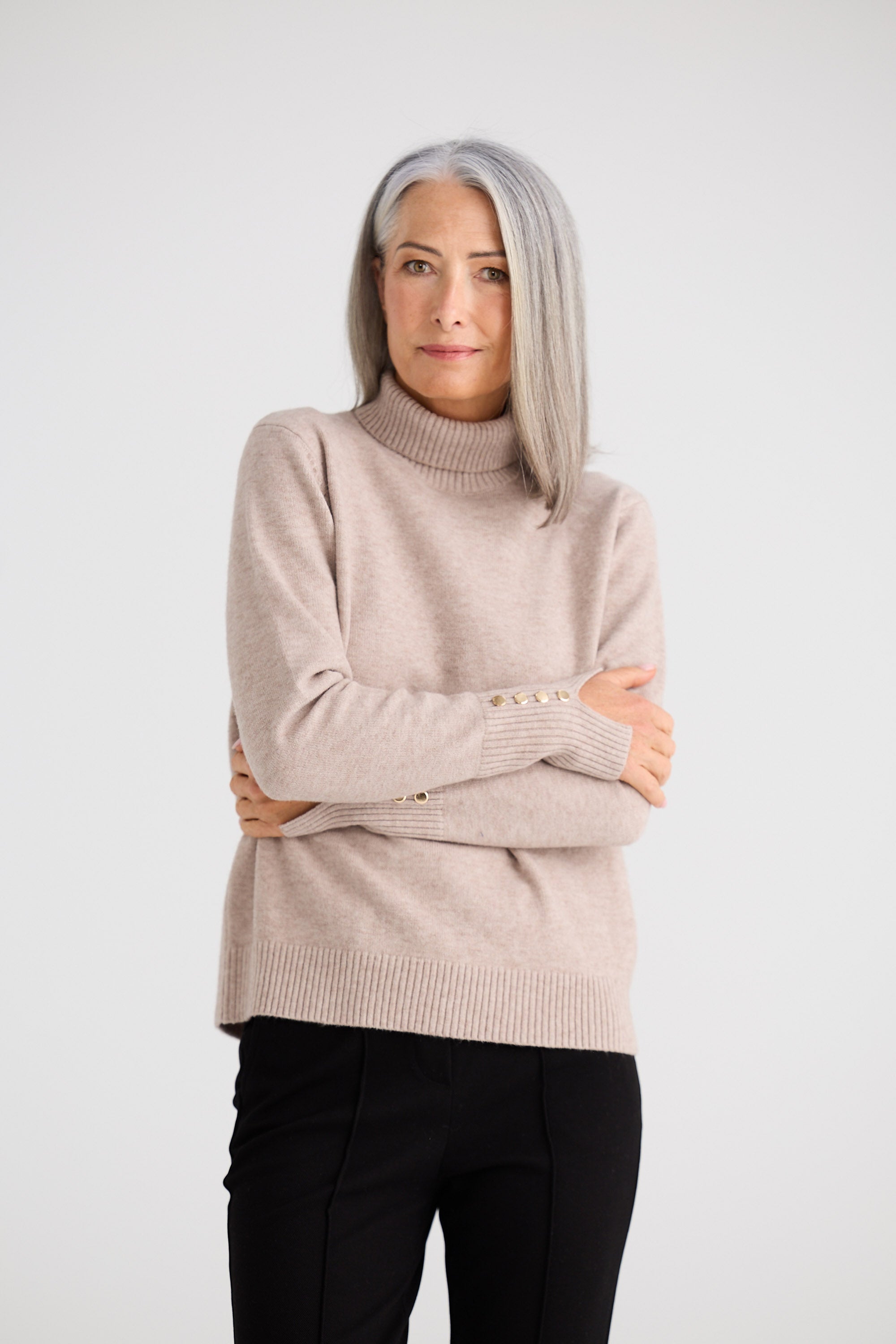 Woman wearing a beige sweater with arms crossed on a white background