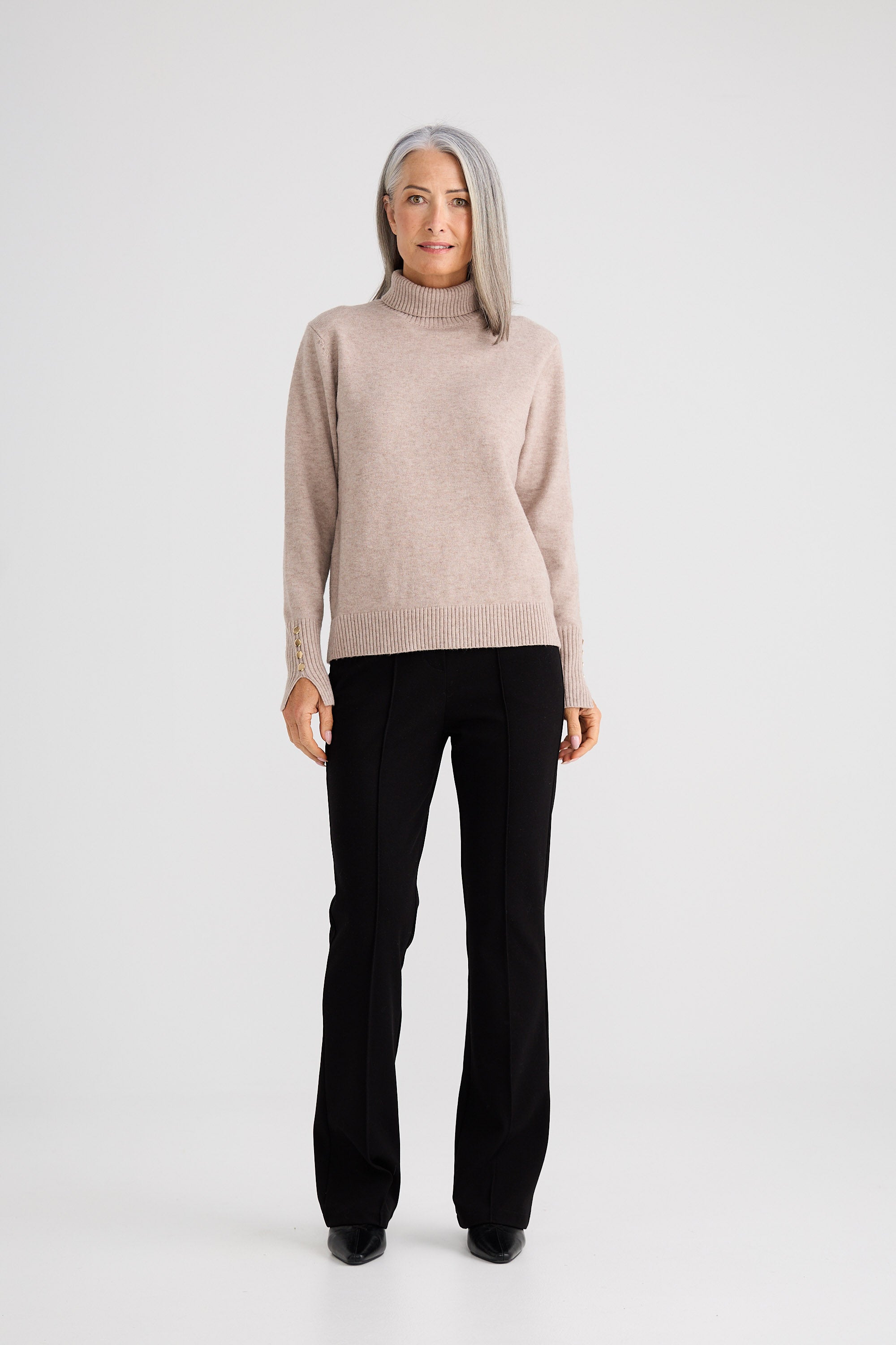 Woman wearing a beige sweater and black pants on a white background