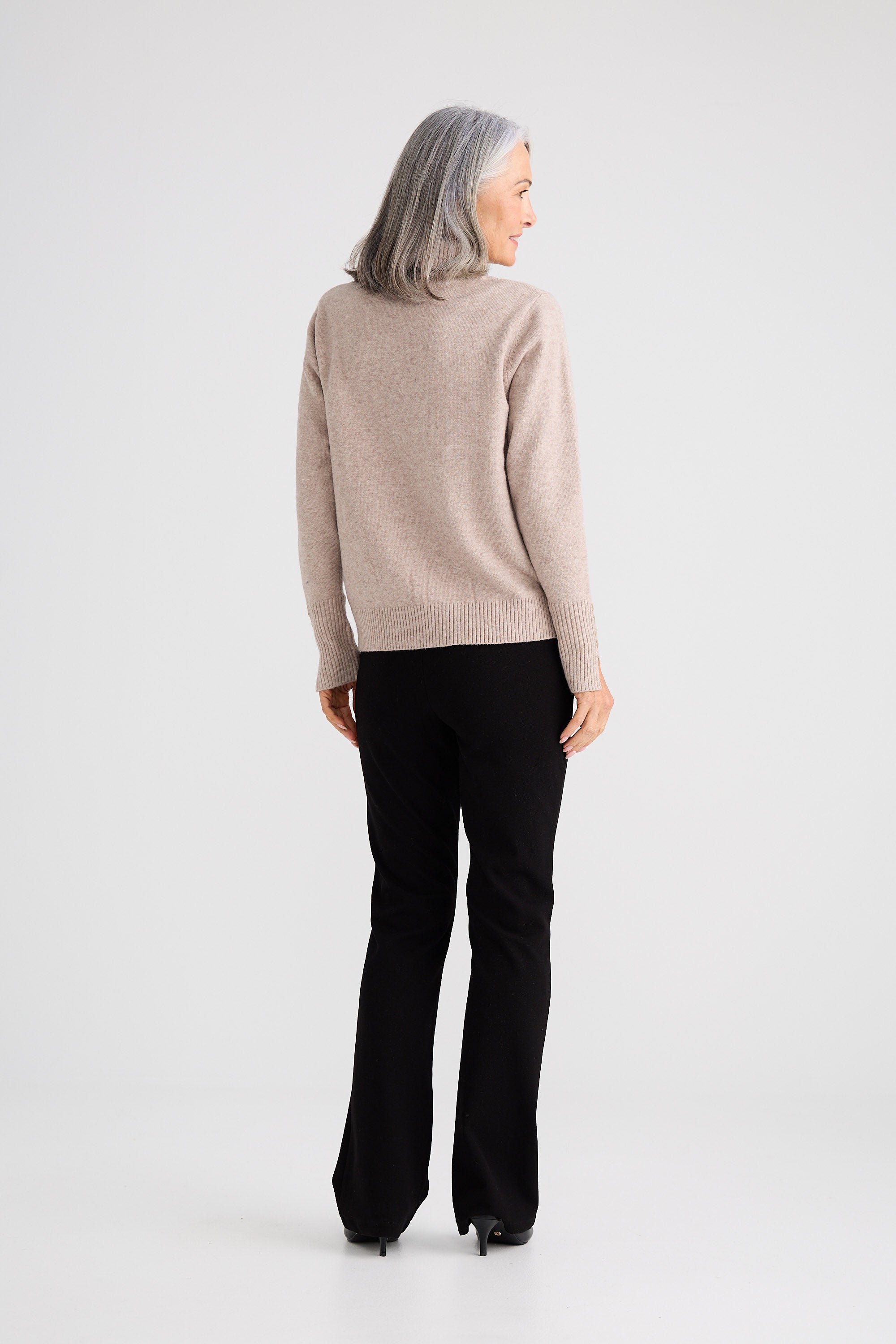 Person wearing a beige sweater and black pants on a white background