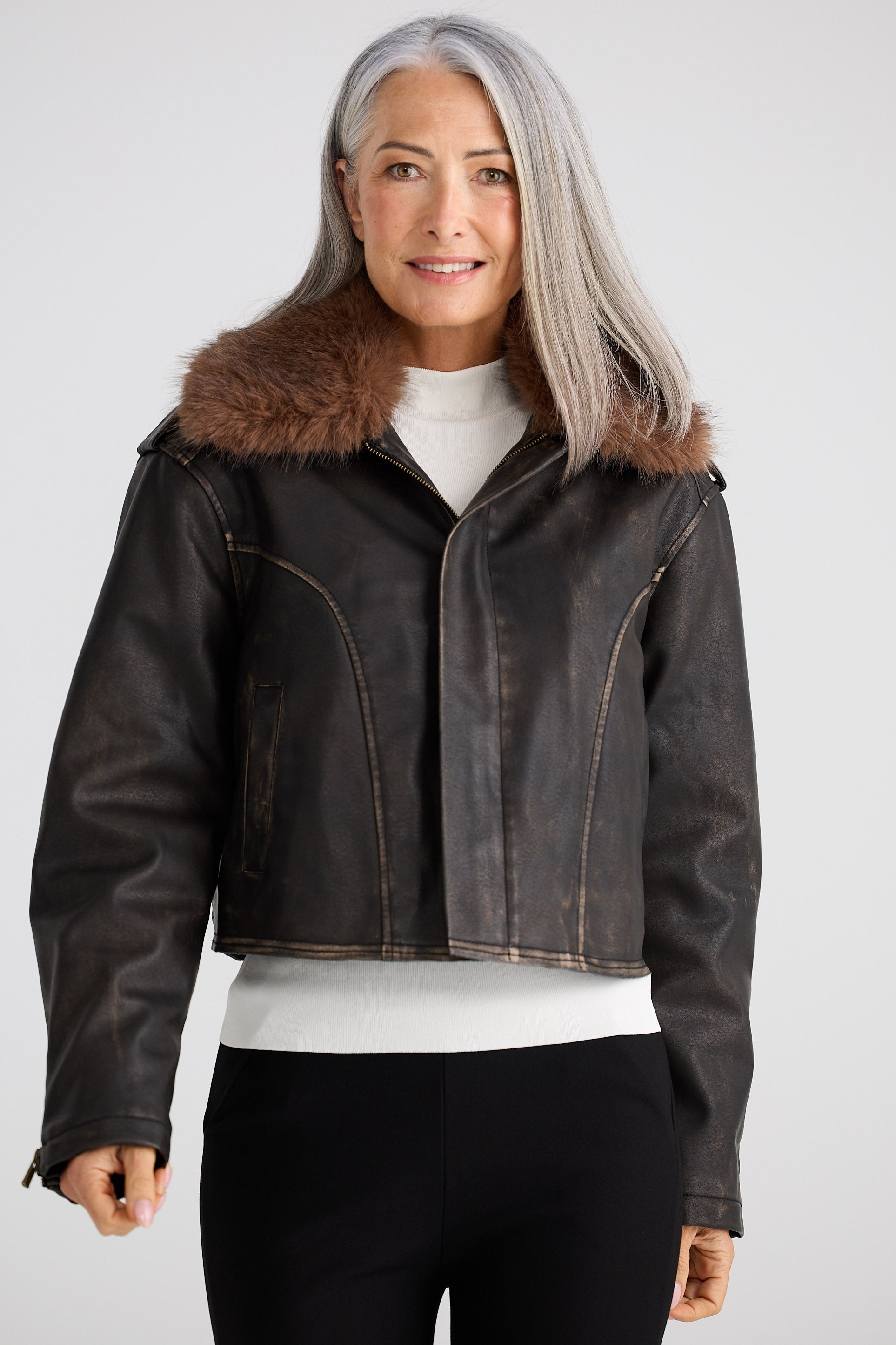 Woman wearing a dark leather jacket with fur collar on a white background