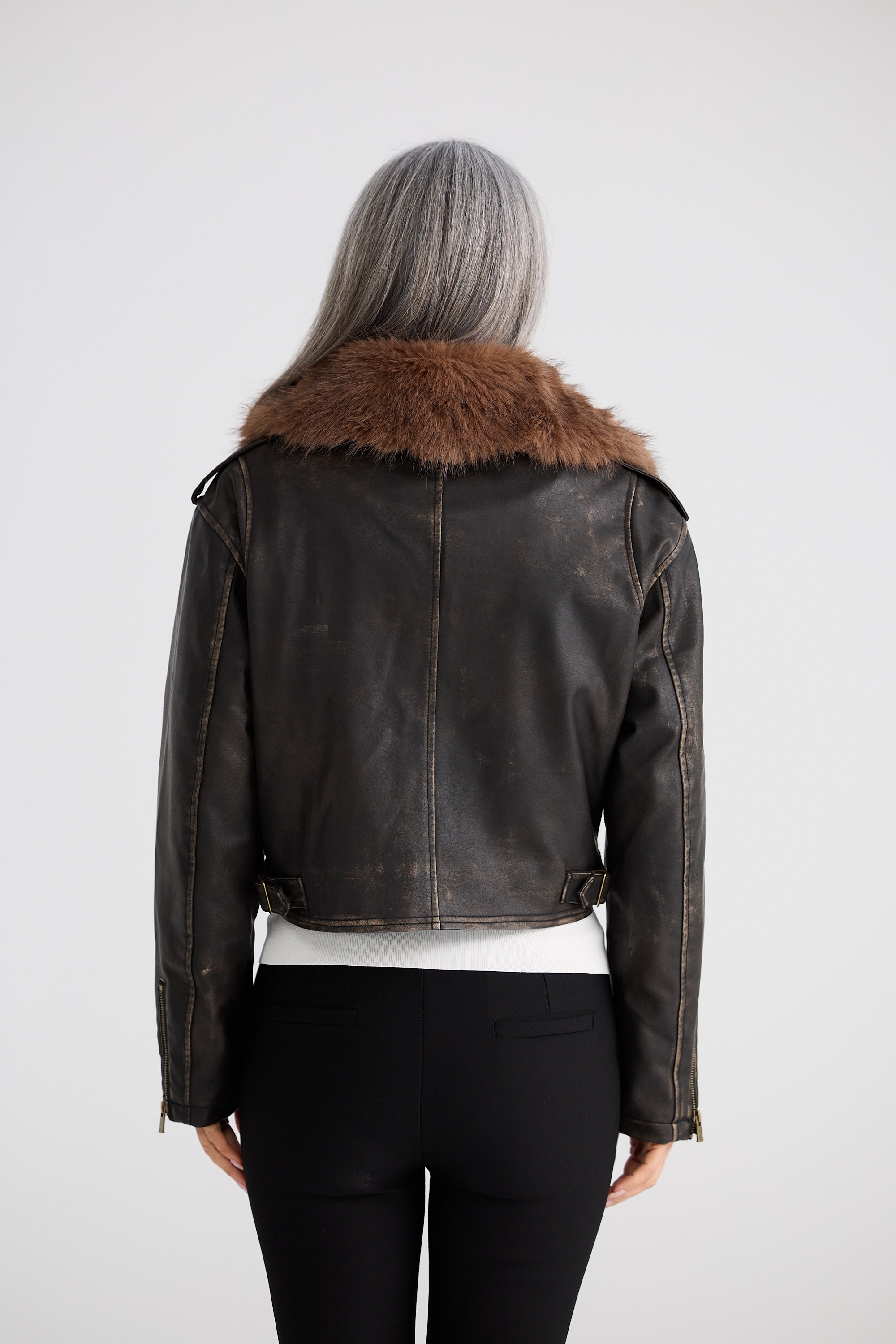 Person wearing a dark leather jacket with fur collar on a plain background