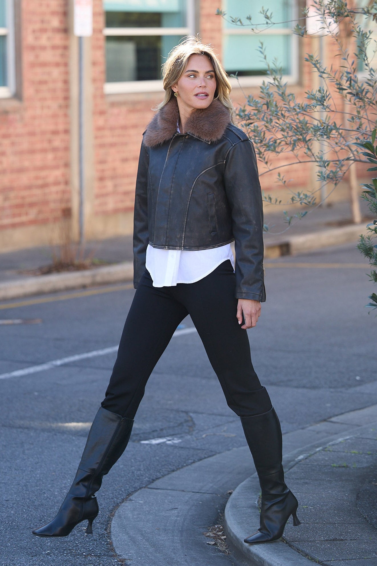 Woman walking on a street wearing a dark jacket and black pants.