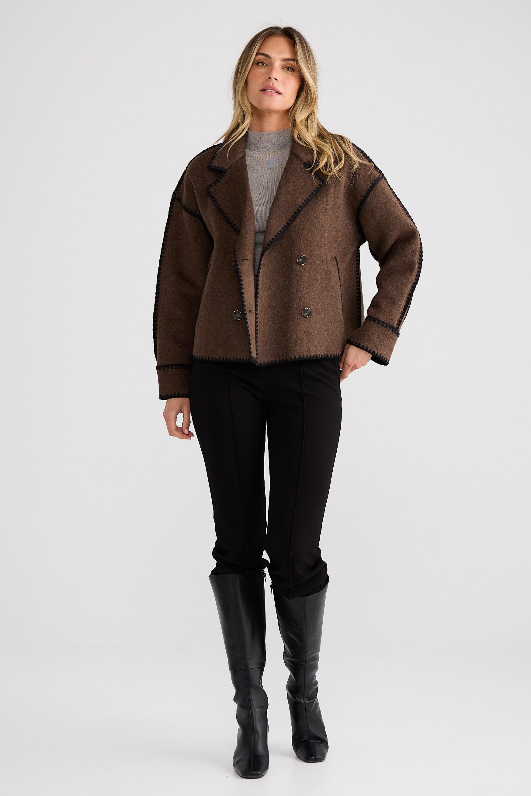 Woman wearing a brown coat, black pants, and black boots on a white background