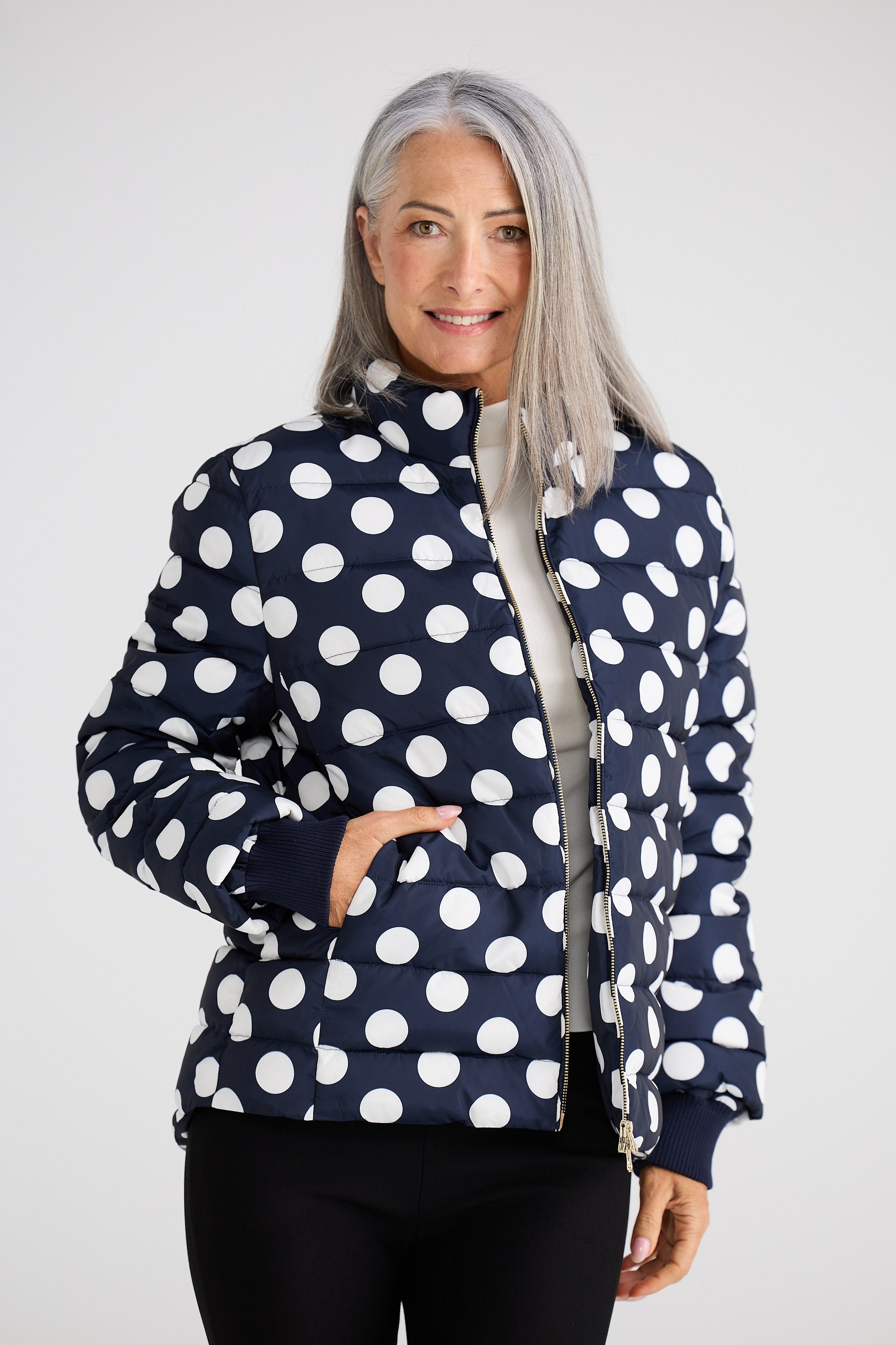 Woman wearing a navy blue jacket with white polka dots on a white background