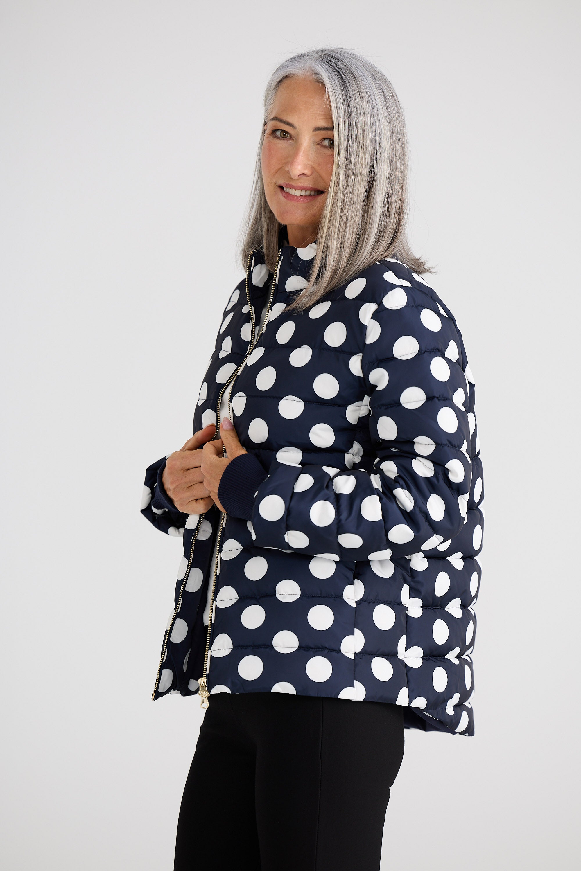 Woman wearing a navy blue puffer jacket with white polka dots on a white background