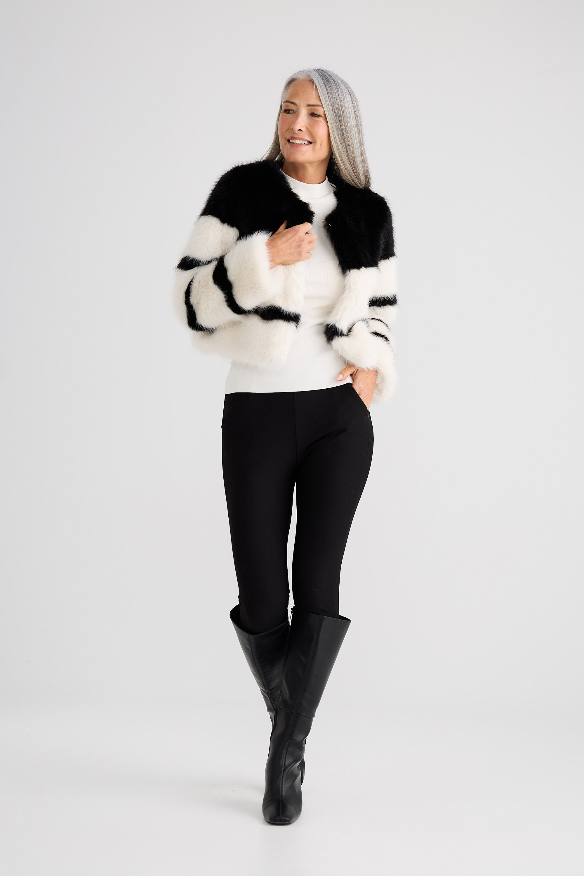 Woman wearing a black and white fur coat, white shirt, black pants, and black boots on a white background