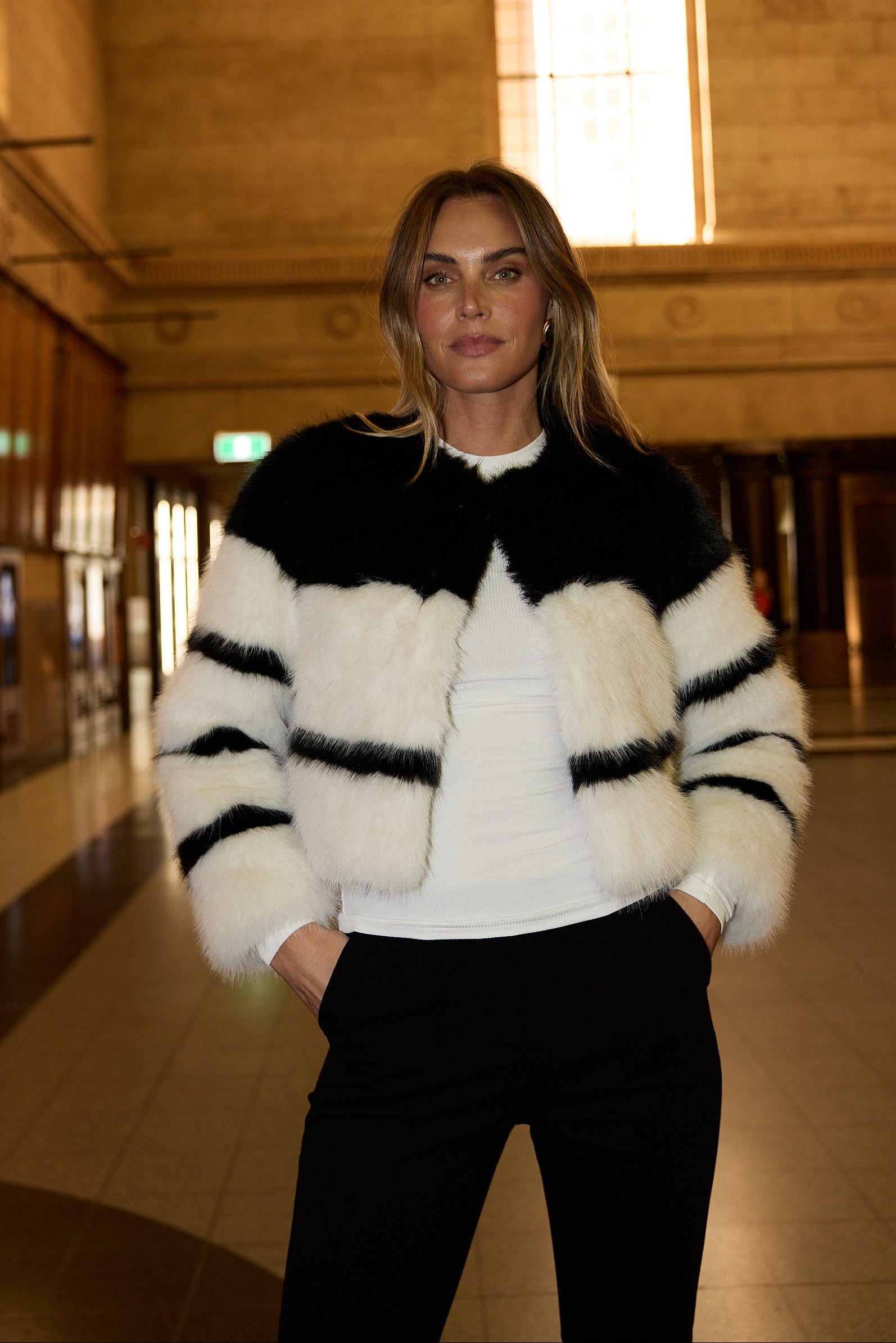 Woman wearing a black and white striped sweater in an indoor setting with large windows.