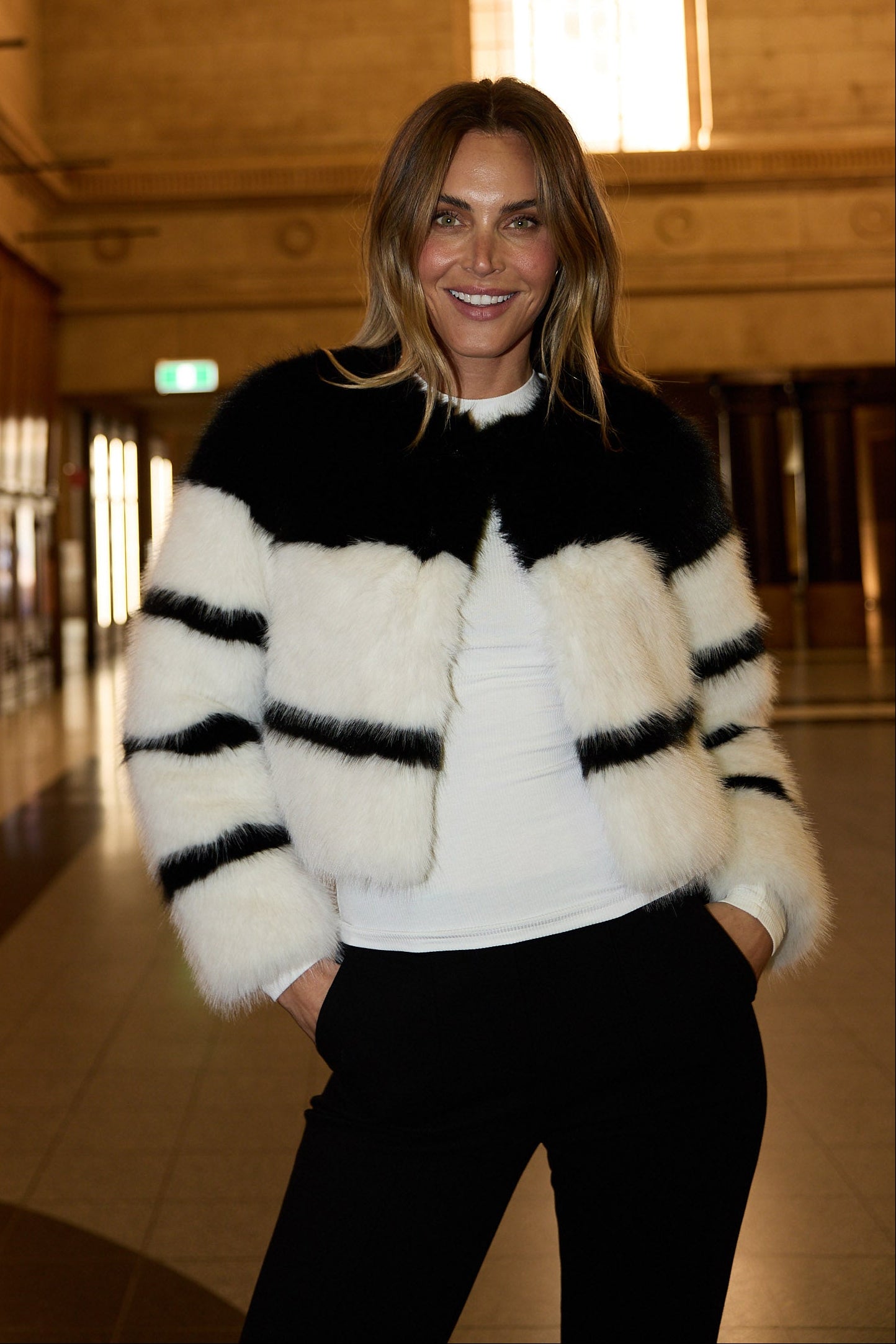 Woman wearing a black and white striped sweater in an indoor setting with large windows.