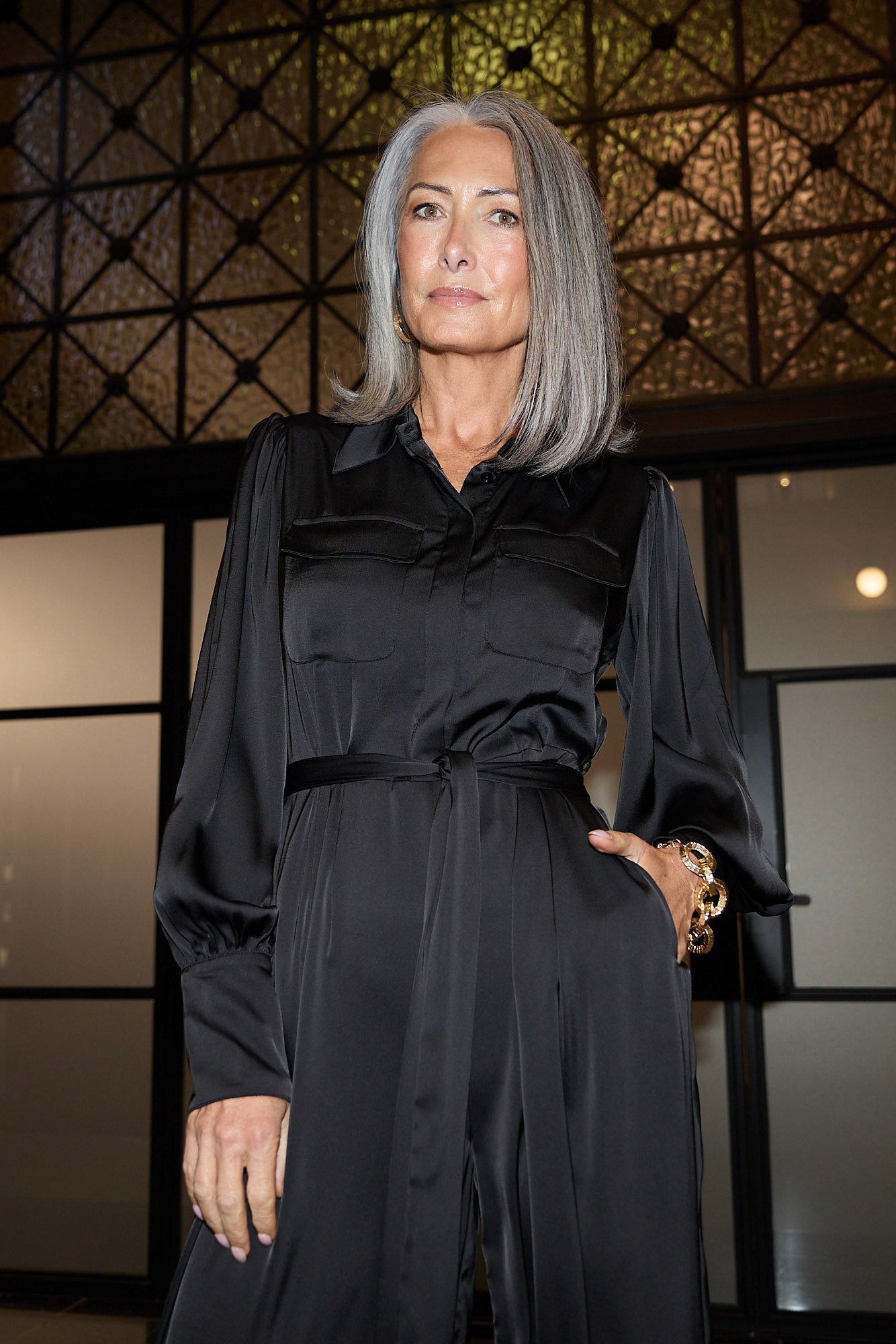 Woman in a black outfit standing in front of a decorative wall.