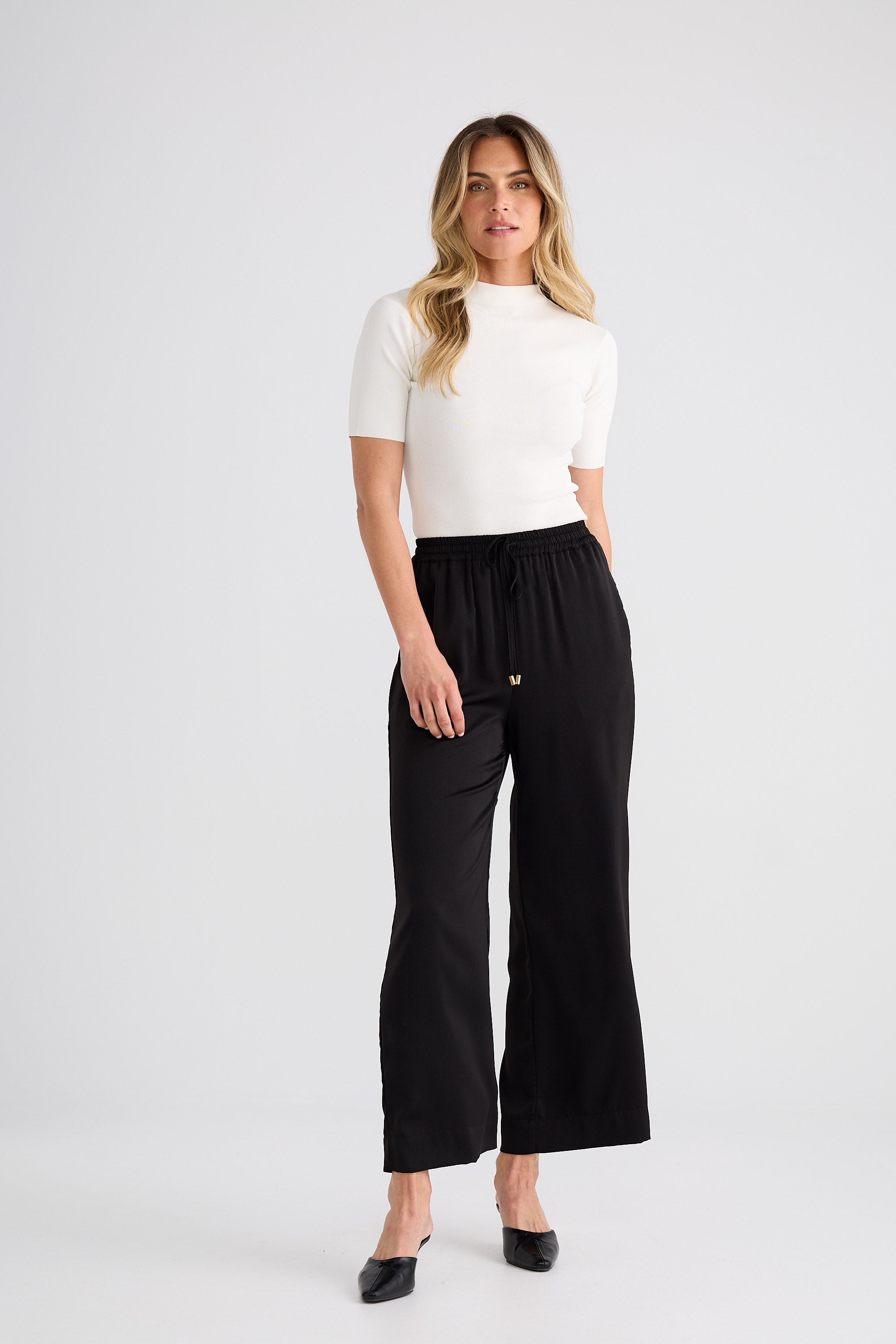 Woman wearing a white top and black wide-leg pants on a white background