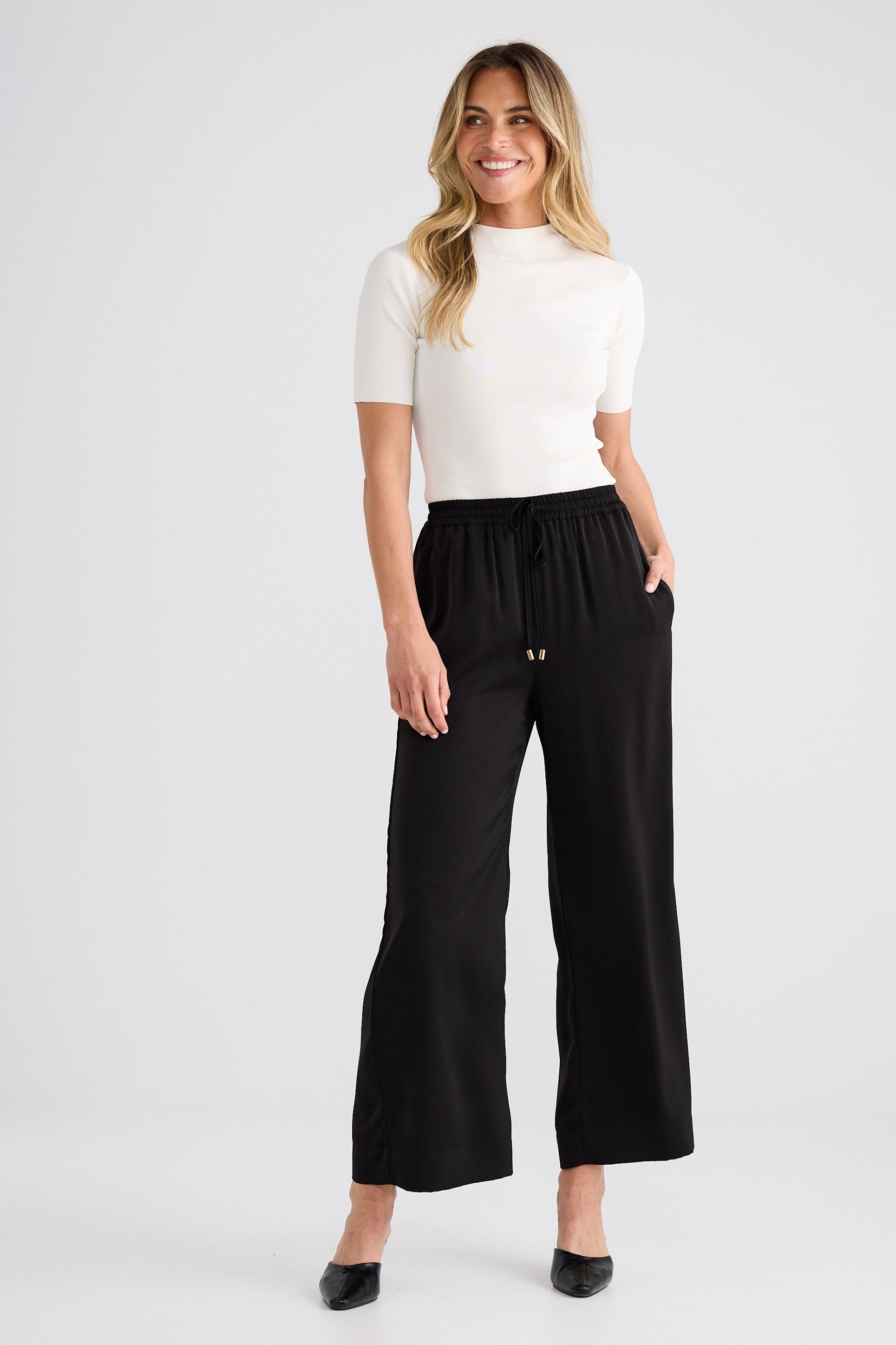 Woman wearing a white top and black wide-leg pants on a white background